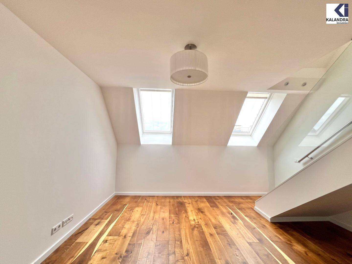 Heller Raum mit Holzboden, Dachfenstern und einer modernen Treppe mit Glasgeländer.