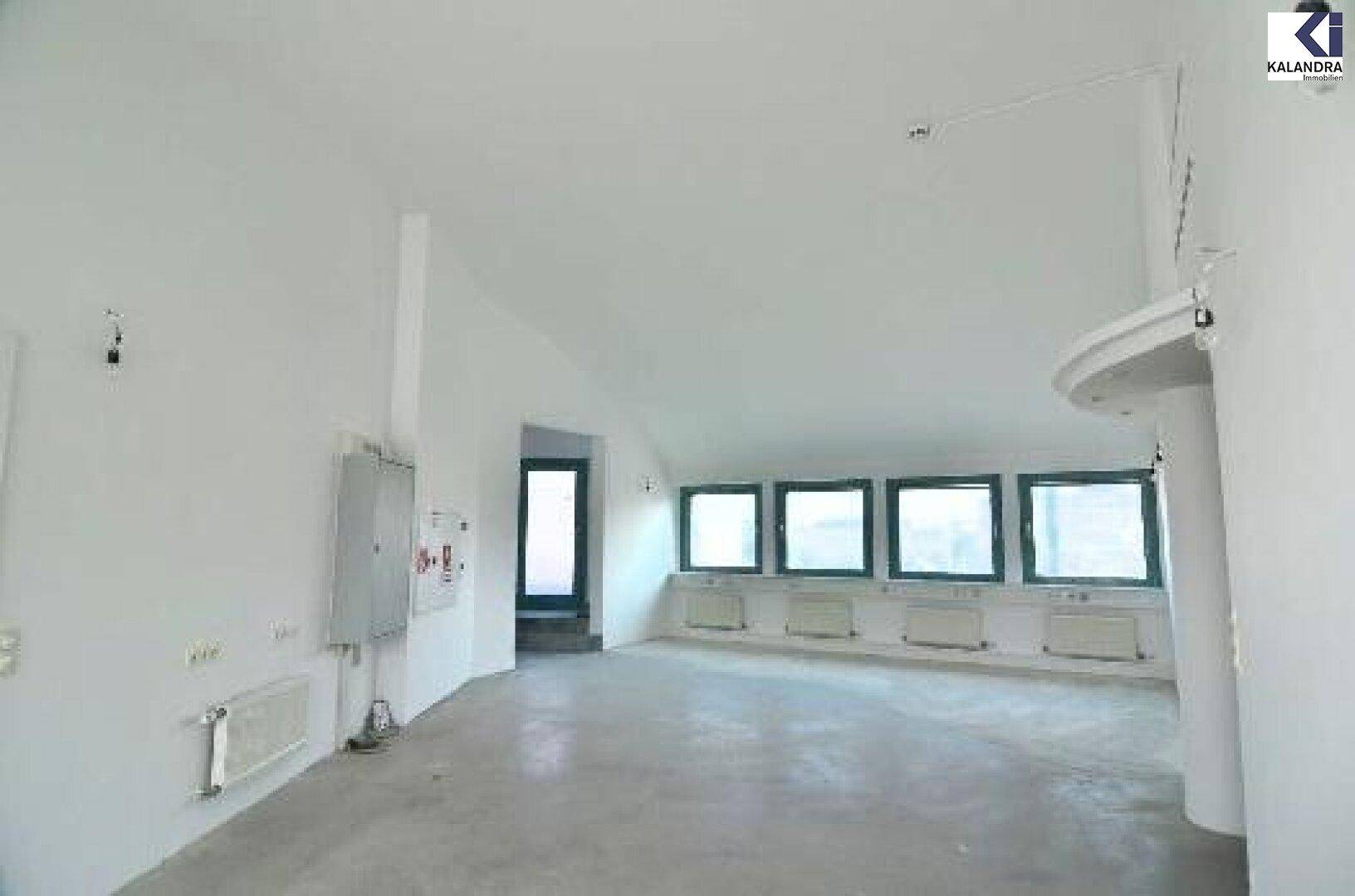 Leerer Raum mit weiß gestrichenen Wänden, Betonboden und einer Reihe kleiner Fenster.