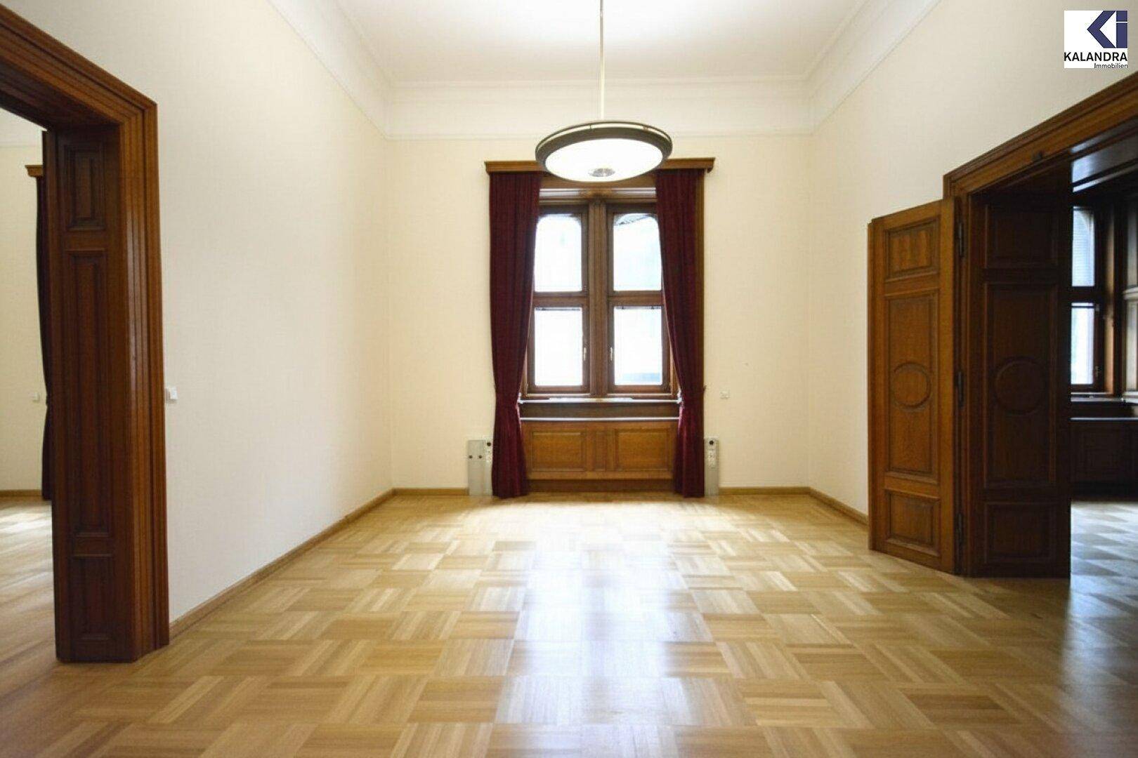 Heller Raum mit Fischgrätparkett, hohen Decken und zwei großen Holztüren, bereit zur Einrichtung.