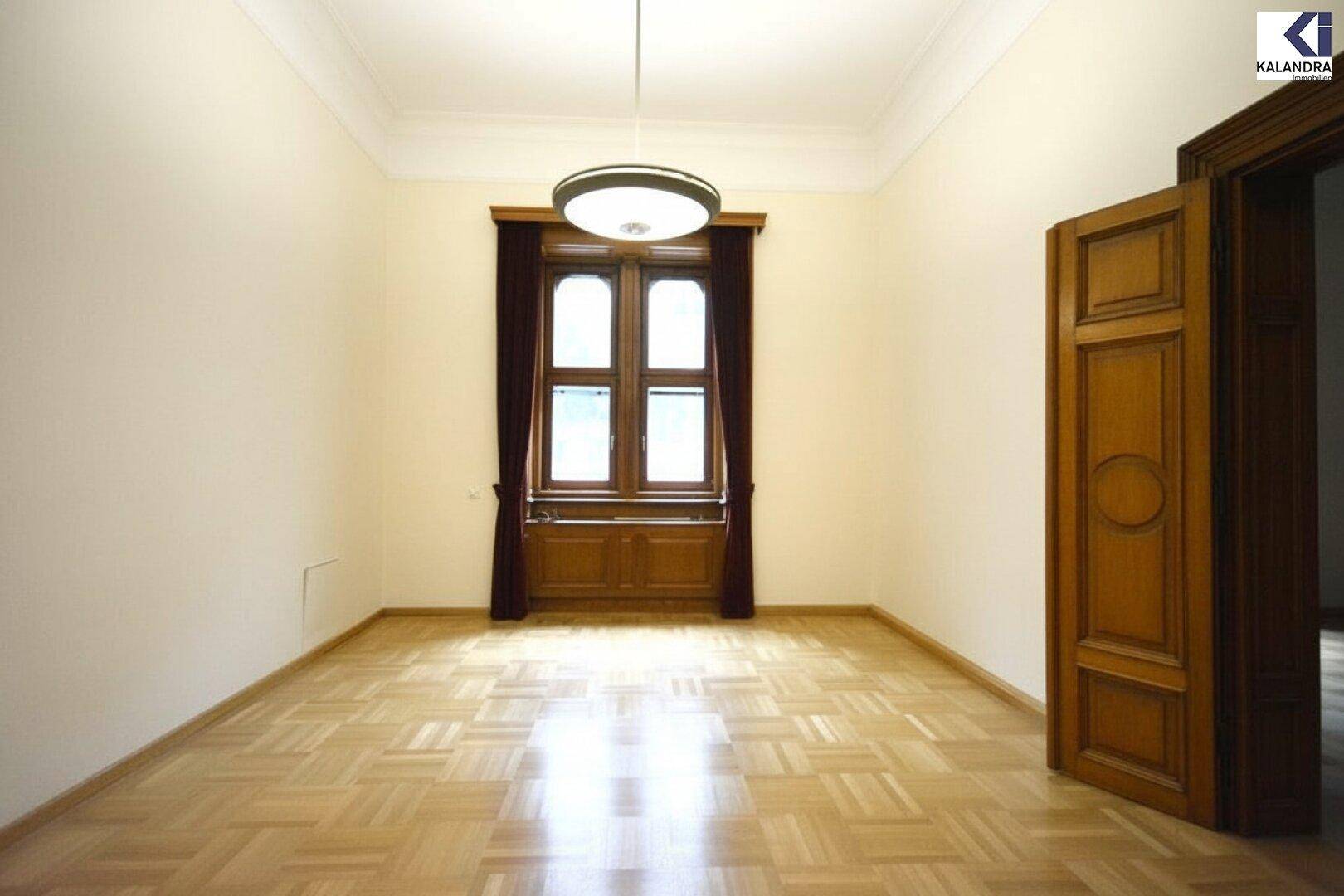 Geräumiger Raum mit hellem Parkettboden, hohen Decken und einer eleganten Holztür im klassischen Stil.
