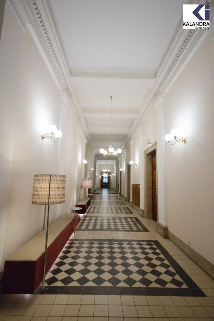 Heller und breiter Flur mit hohen Stuckdecken, eleganten Wandleuchten und gemustertem Fliesenboden.