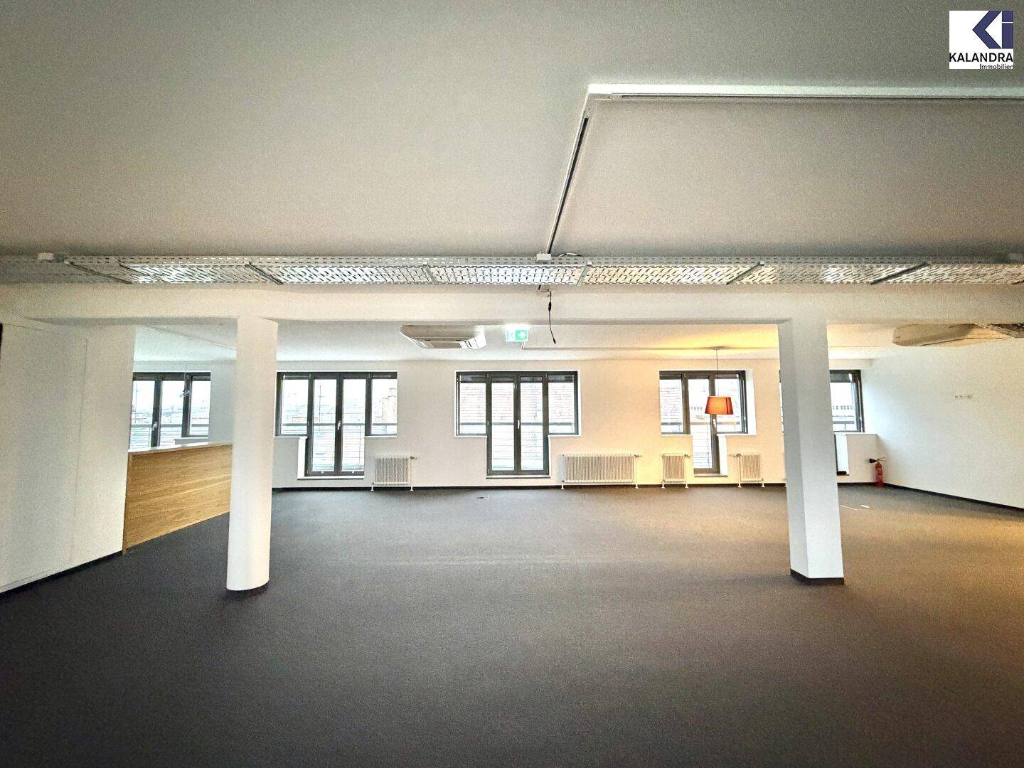 Weitläufiger Bürobereich mit Teppichboden, mehreren Fenstern und einer modernen Deckenbeleuchtung.