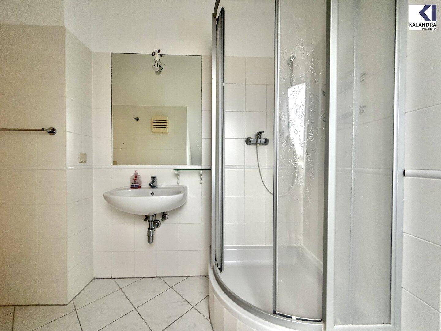 Funktionales Badezimmer mit Duschkabine, Waschbecken und weißen Fliesen an Wänden und Boden.