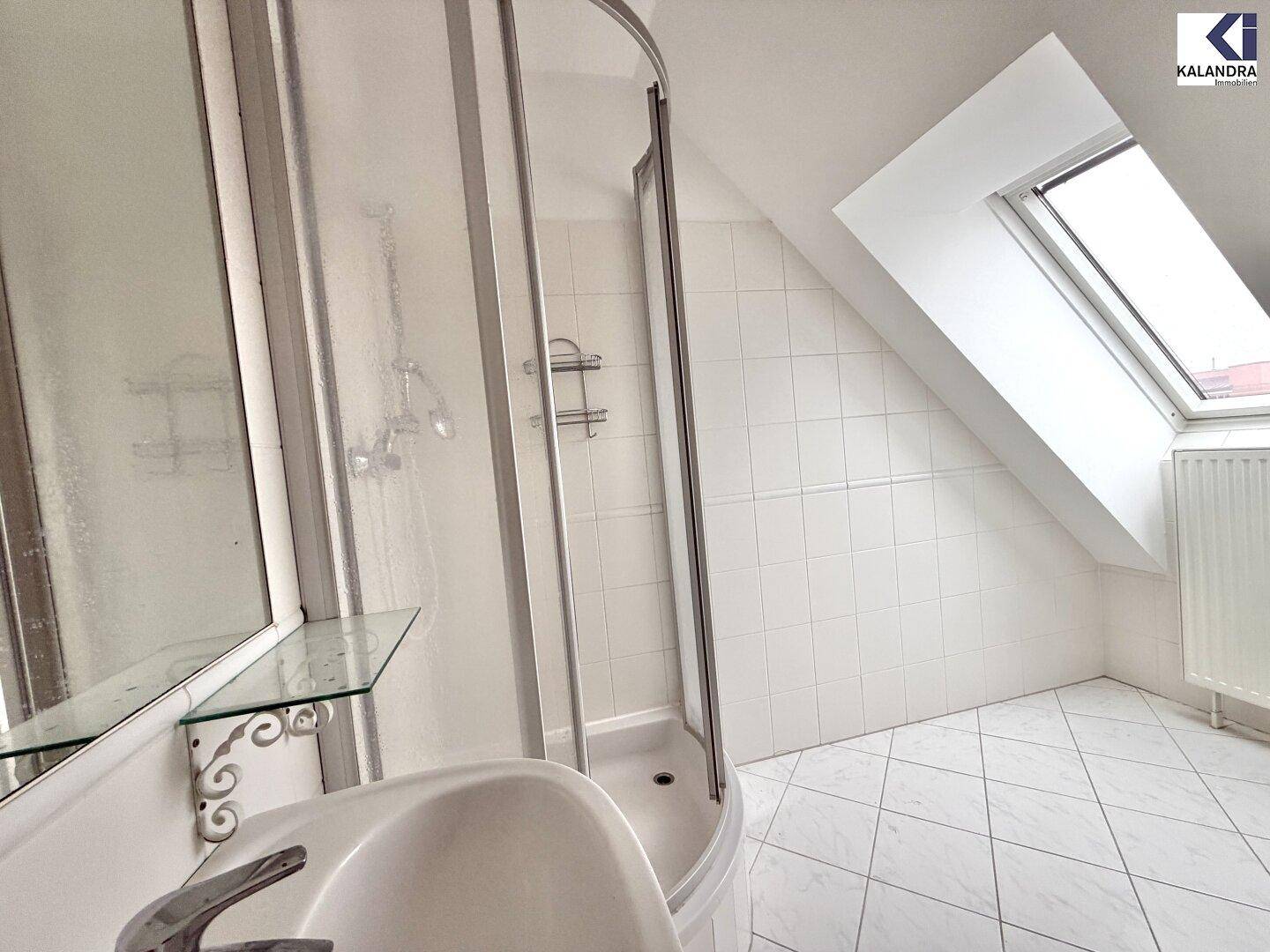 Helles Badezimmer im Dachgeschoss mit Duschkabine, Waschbecken und schrägem Dachfenster.