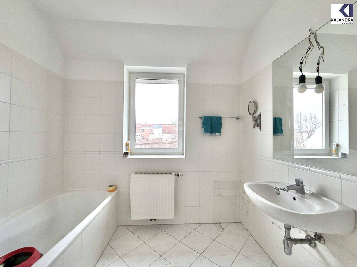 Geräumiges Badezimmer mit Badewanne, Waschbecken, großem Spiegel und Fenster für Tageslicht.