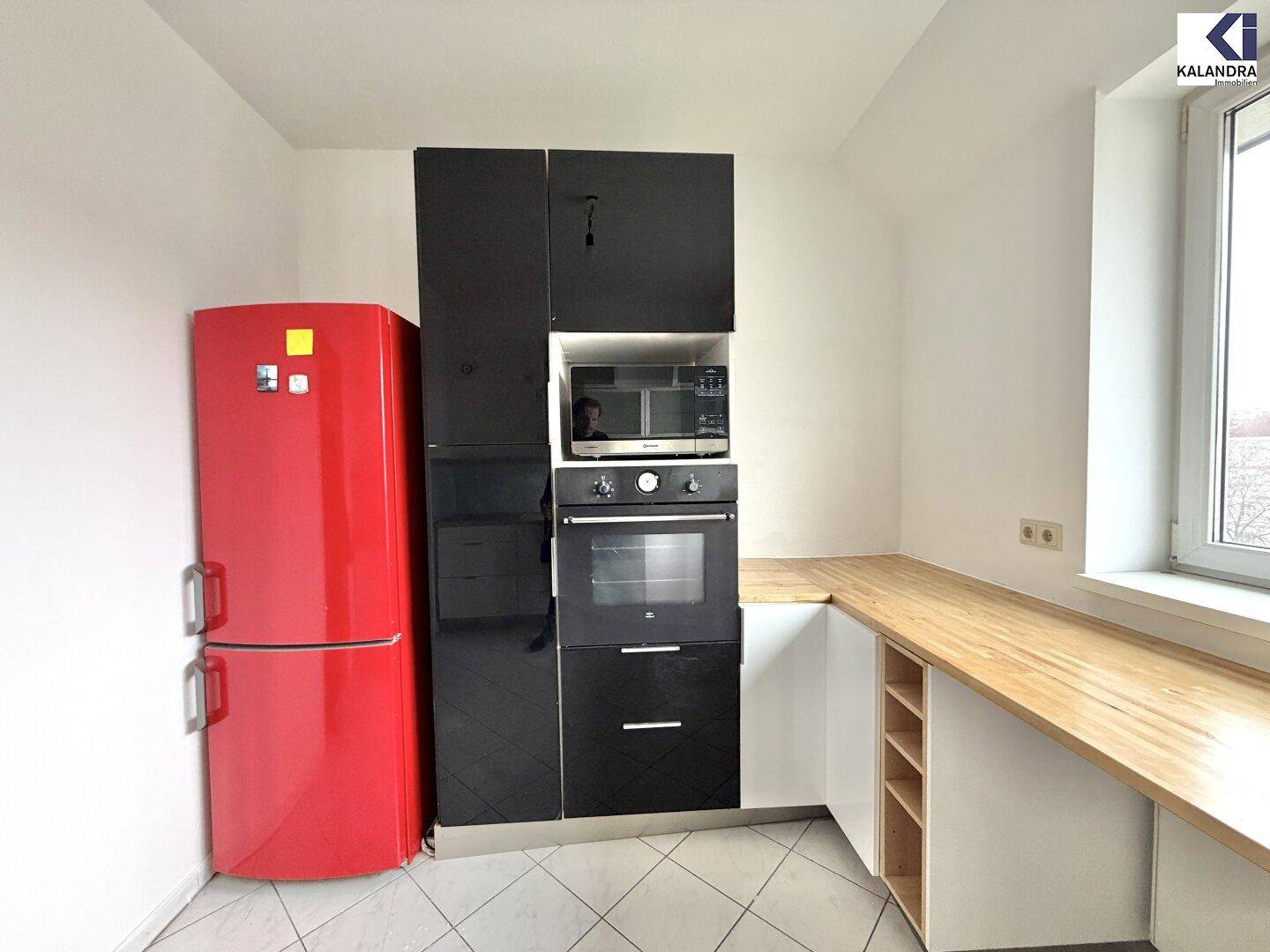 Moderne Küche mit schwarzen Hochglanzschränken, Holzarbeitsplatte und auffälligem rotem Kühlschrank.