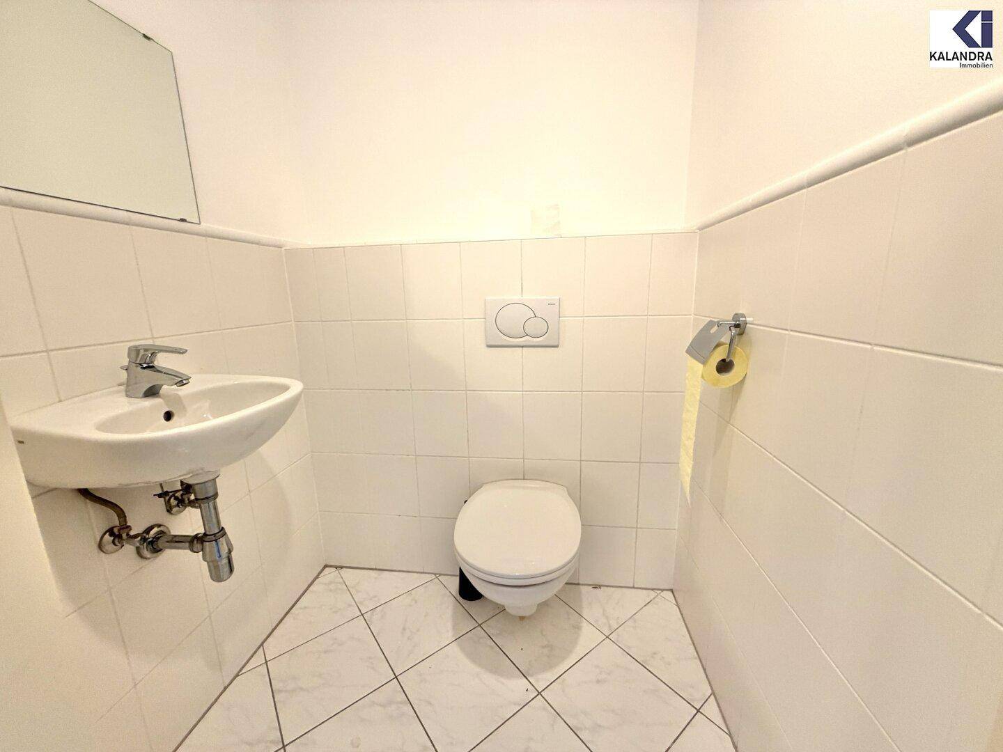 Kleines Gäste-WC mit wandmontierter Toilette, Waschbecken und weißen Fliesen.