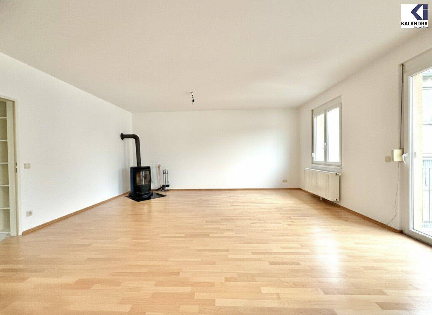 Helles, leeres Wohnzimmer mit hellem Parkettboden und einem modernen Holzofen.