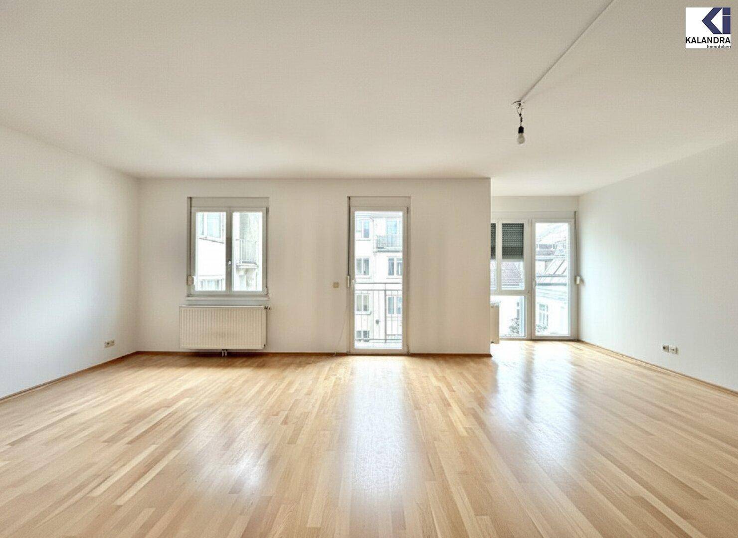 Lichtdurchflutetes Wohnzimmer mit Parkettboden und Zugang zu einem kleinen Balkon.