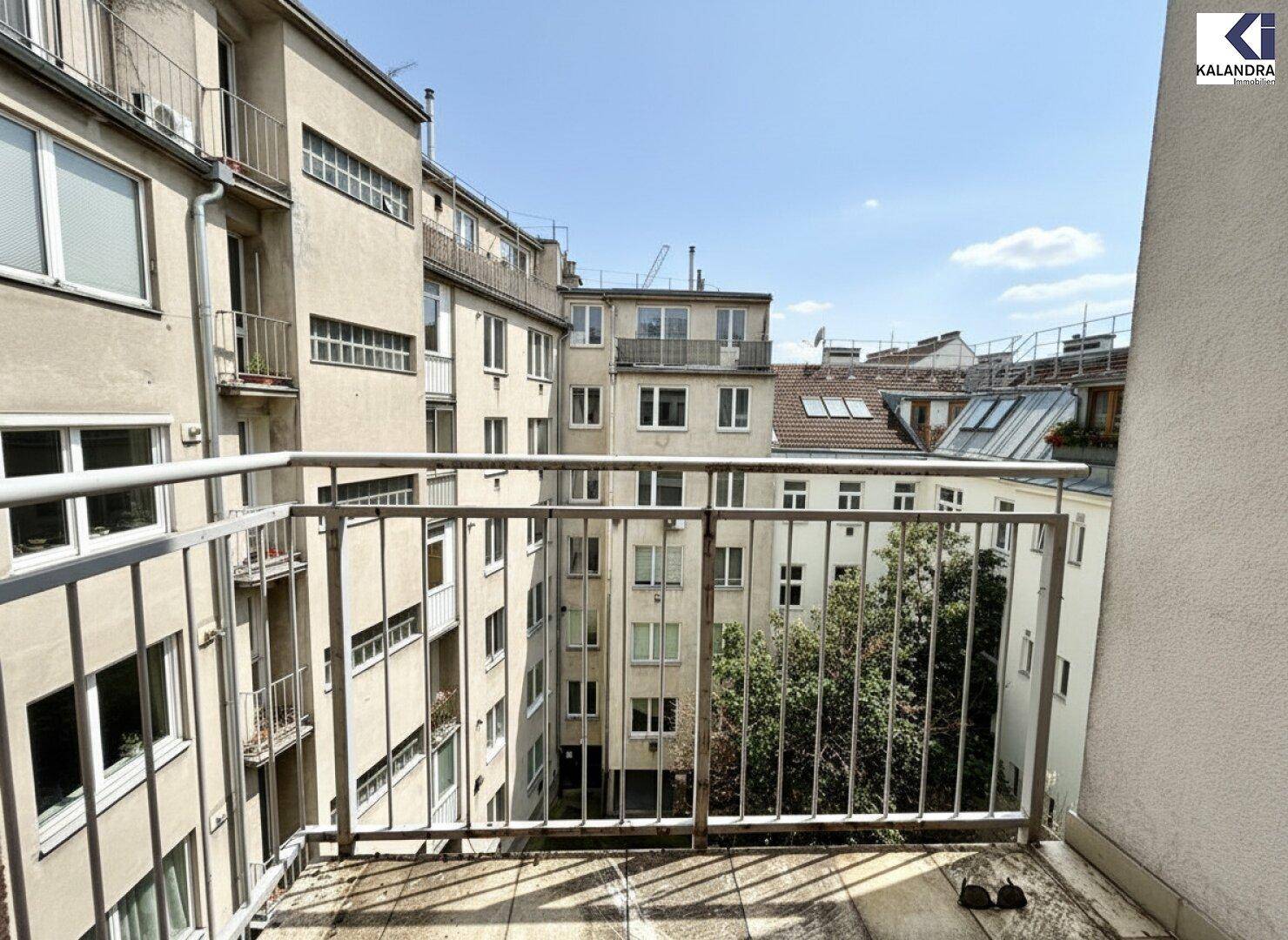 Kleiner Balkon mit Metallgeländer und Blick auf den begrünten Innenhof der Wohnanlage.