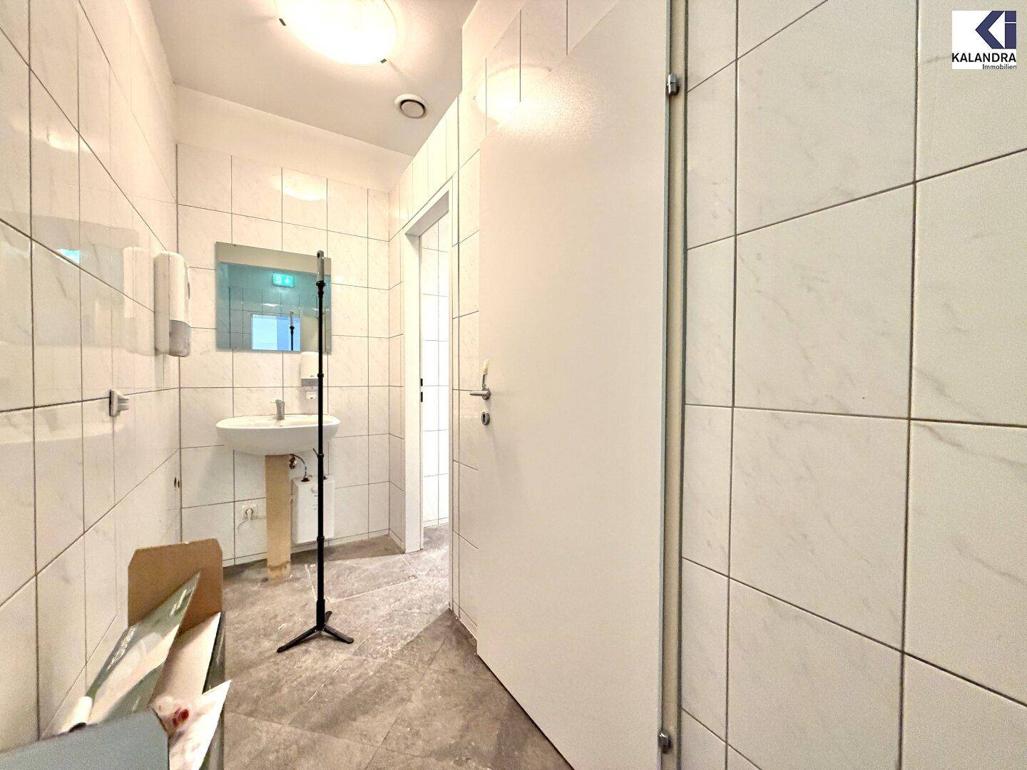 Sauberer Toilettenraum mit weißen Fliesen, Waschbecken und Spiegel, in gutem Zustand.