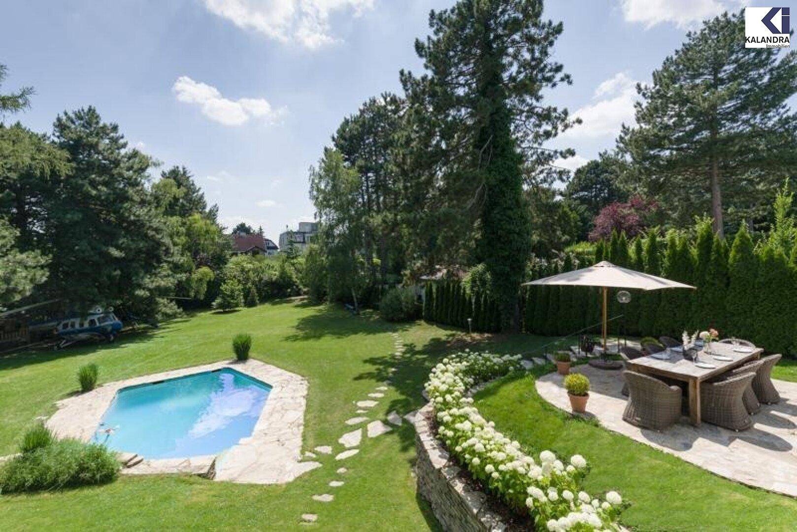 Weitläufiger Garten mit Pool, Essbereich und altem Baumbestand unter blauem Himmel.
