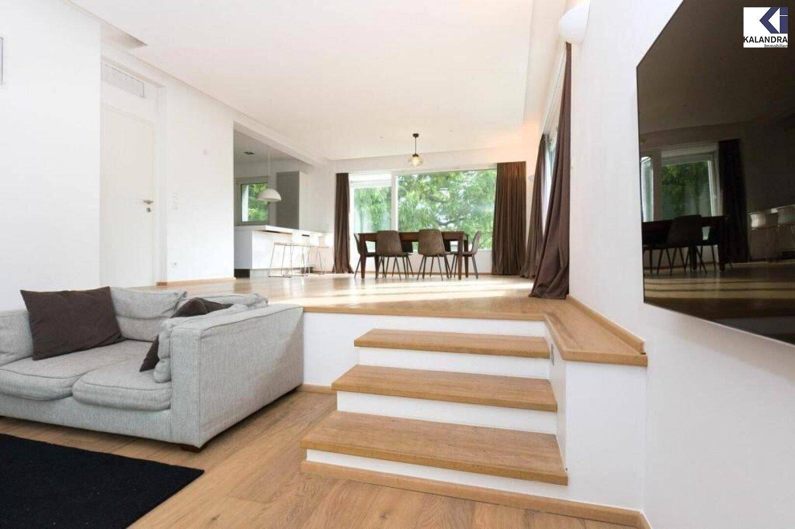 Offener Wohnbereich mit Stufen zum erhöhten Esszimmer und Blick auf den Garten.