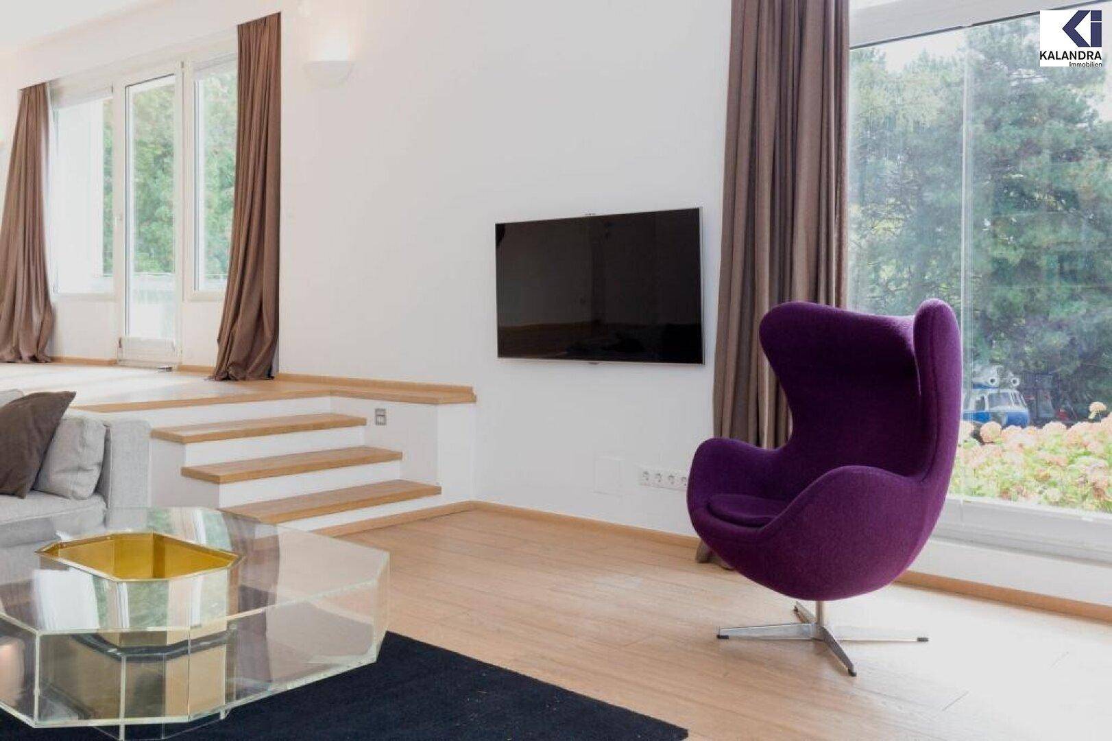 Heller Wohnbereich mit Parkettboden, modernem Sessel und großem Fenster zum Garten.