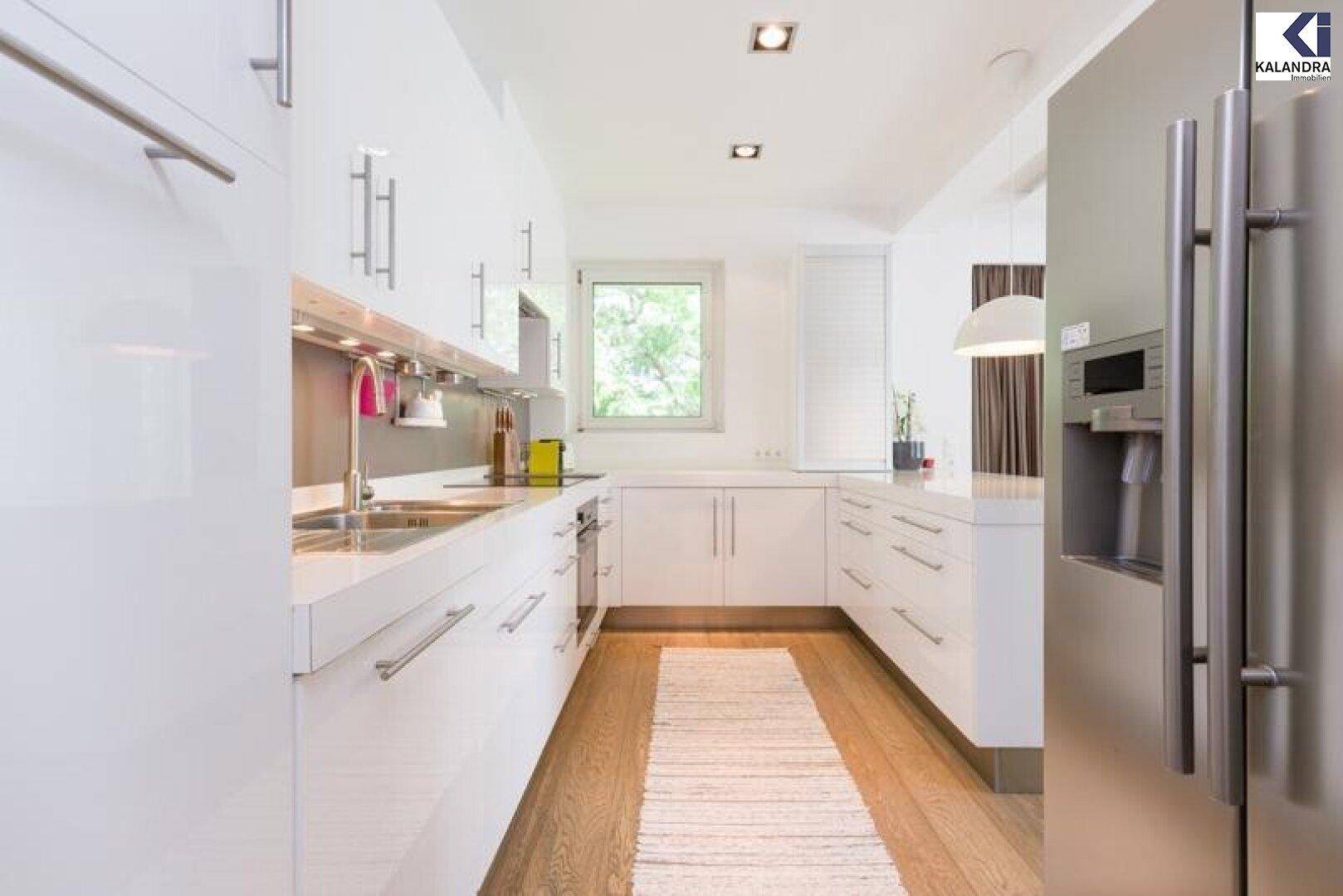 Moderne weiße Küche mit Hochglanzfronten, integrierten Geräten und Fenster.