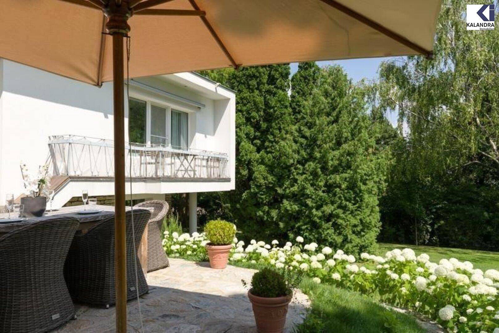Gemütlicher Essbereich auf der Terrasse mit Sonnenschirm und Blick auf den Garten.
