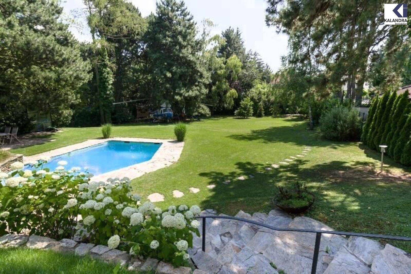 Weitläufiger Garten mit Pool, Steintreppe und blühenden Sträuchern unter blauem Himmel.
