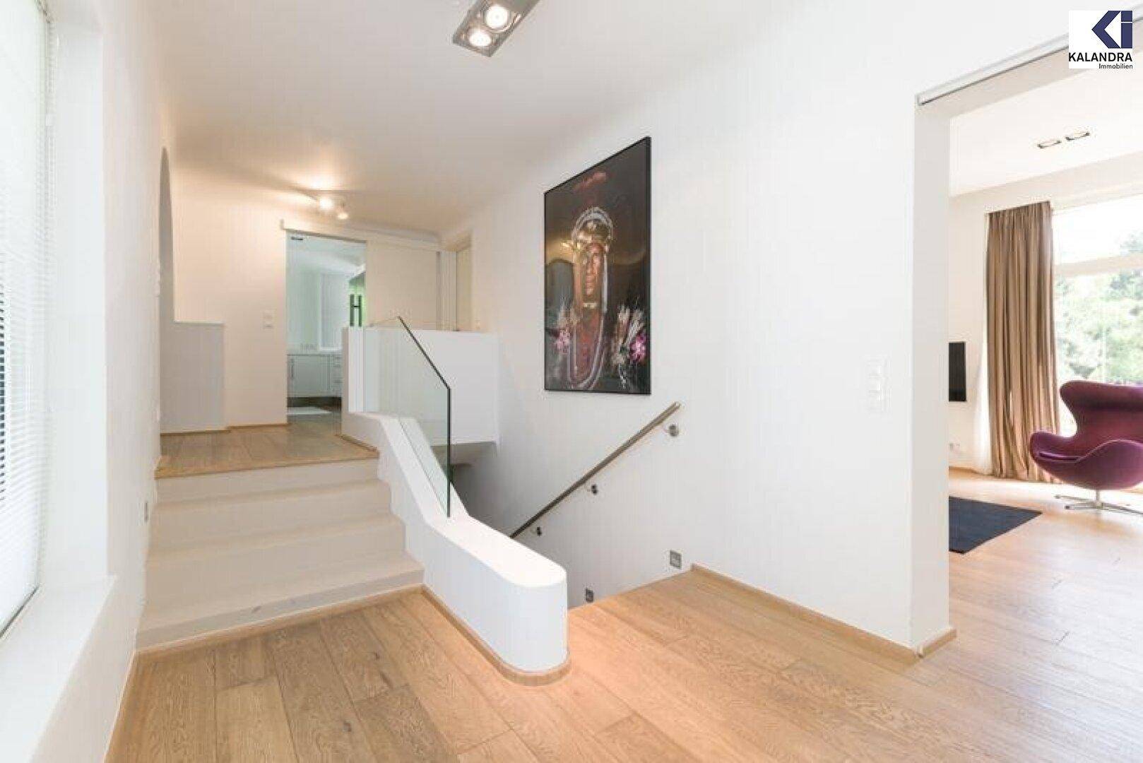 Heller Flur mit Holzparkett, moderner Treppe und Kunstwerk an der Wand.