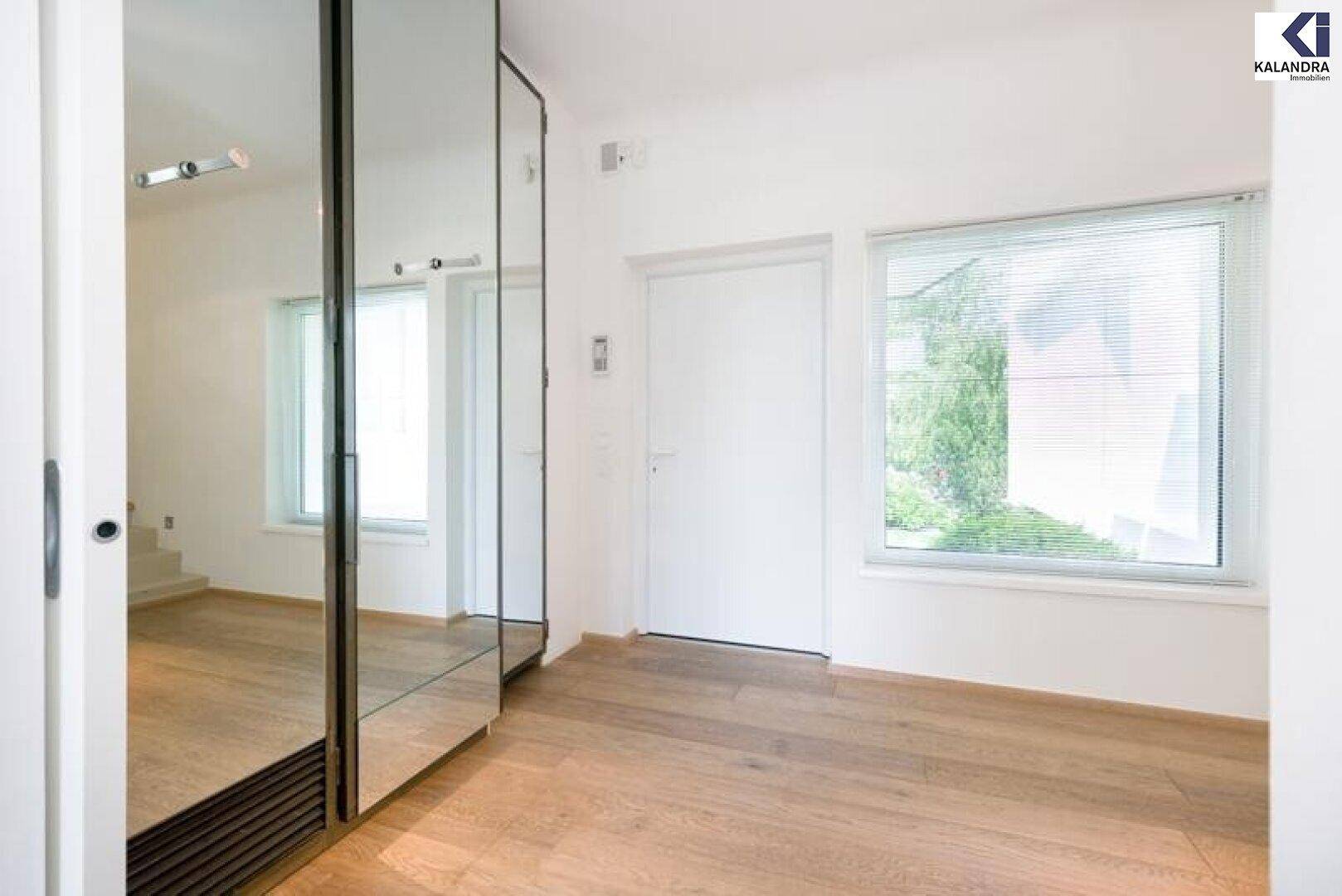 Heller Flur mit Parkettboden, Spiegelschrank und Fenster mit Blick ins Grüne.