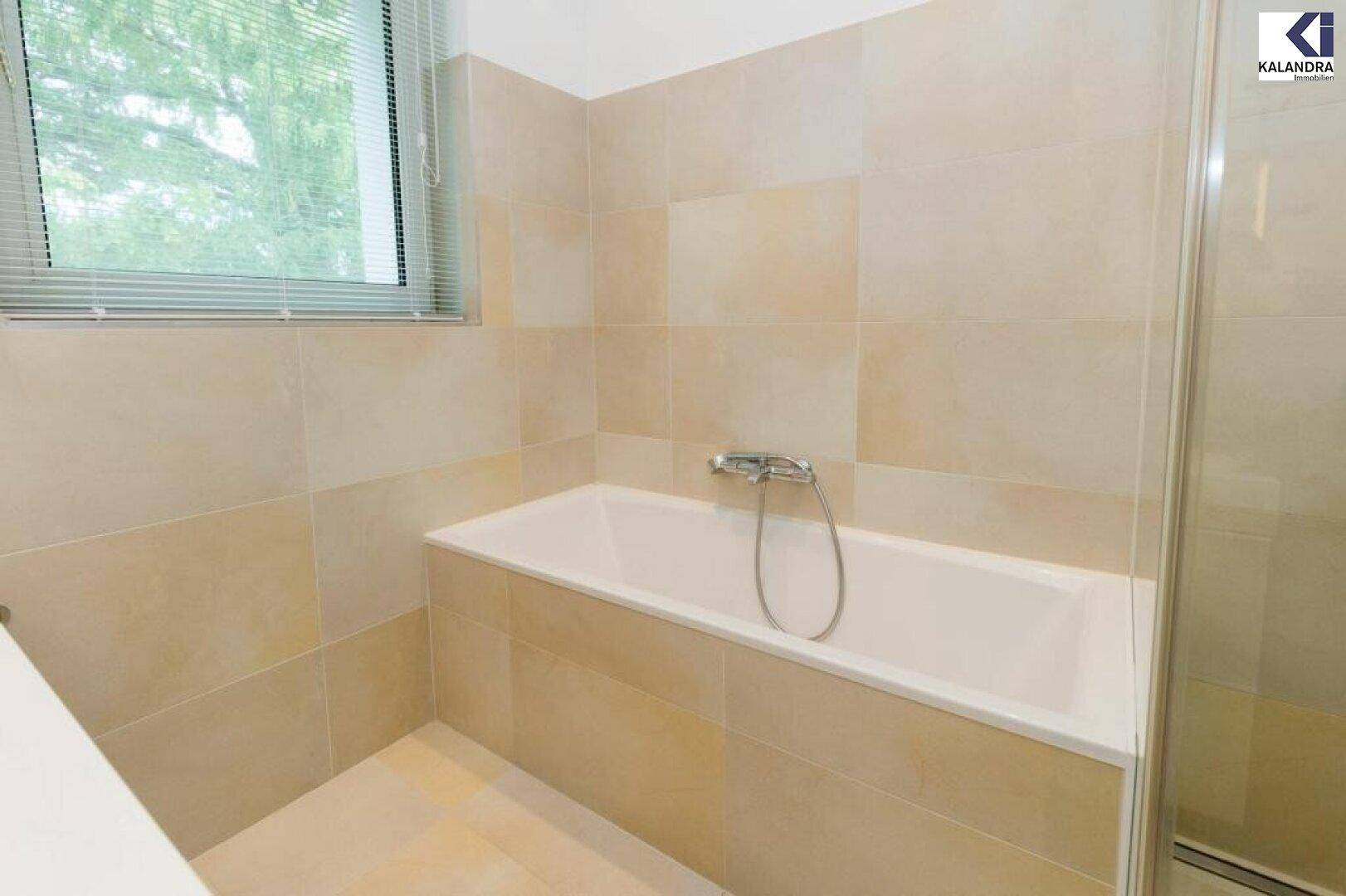 Helles Badezimmer mit Badewanne, beigefarbenen Fliesen und Fenster.