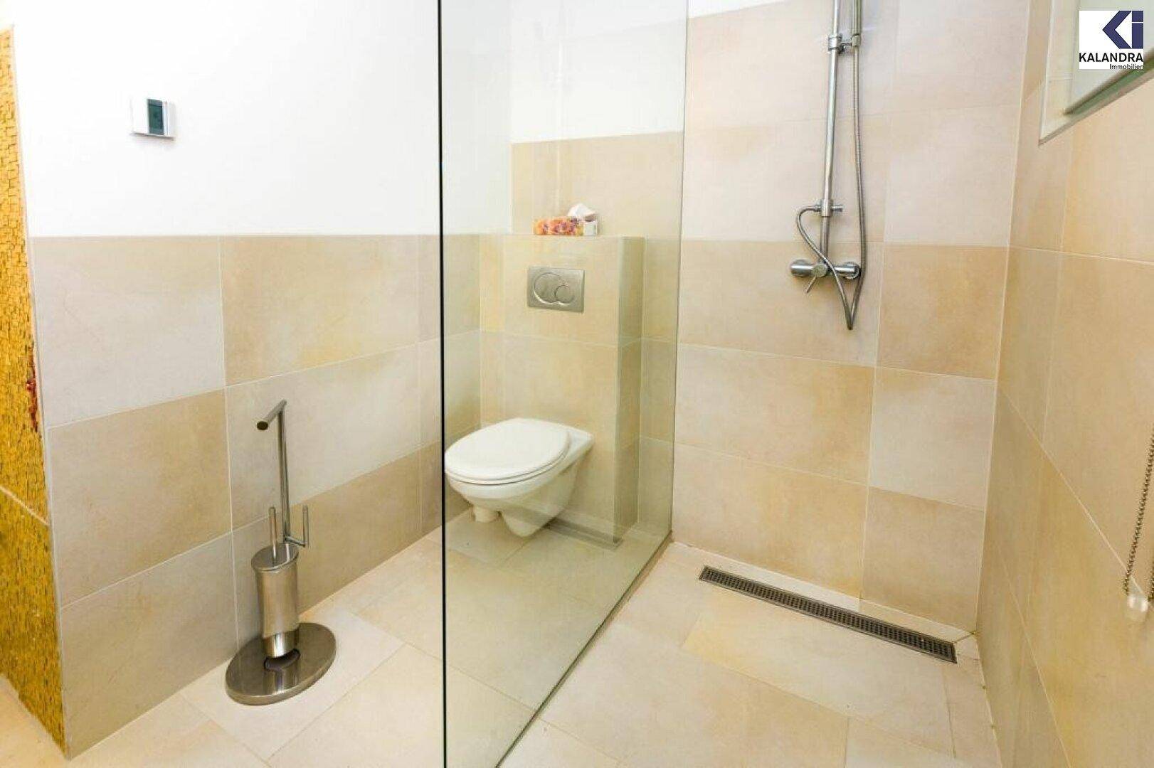 Modernes WC mit wandmontierter Toilette und ebenerdiger Dusche.