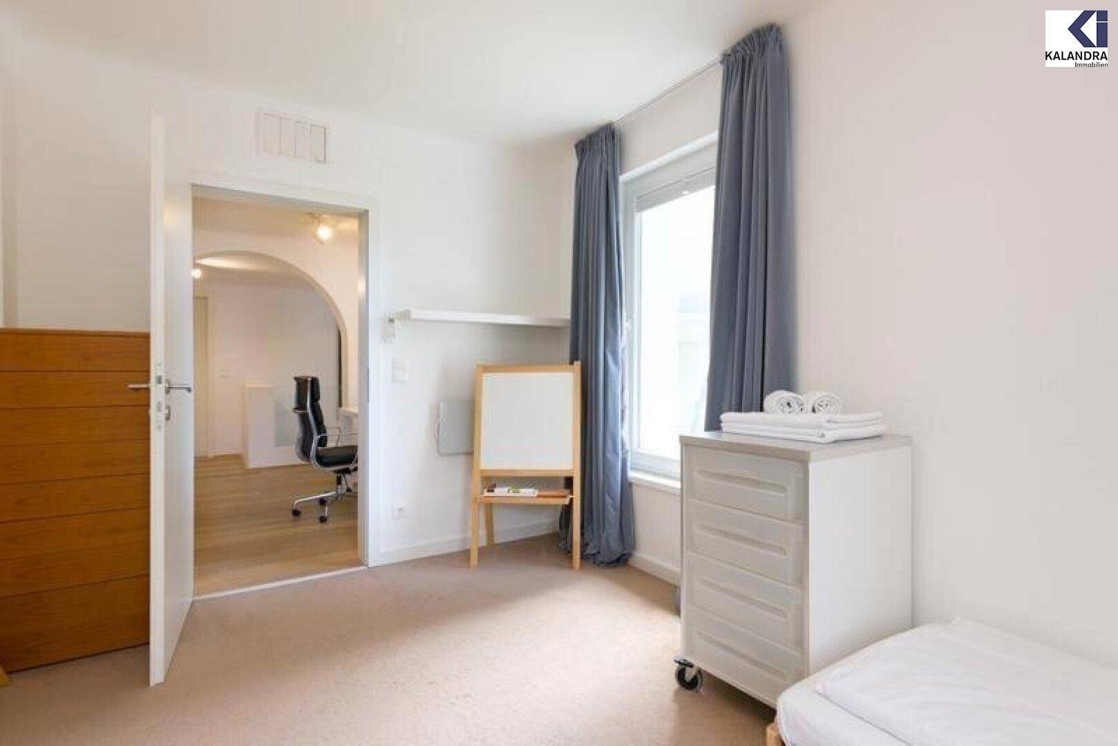 Helles Zimmer mit Teppichboden, Fenster und offenem Zugang zu einem weiteren Raum.