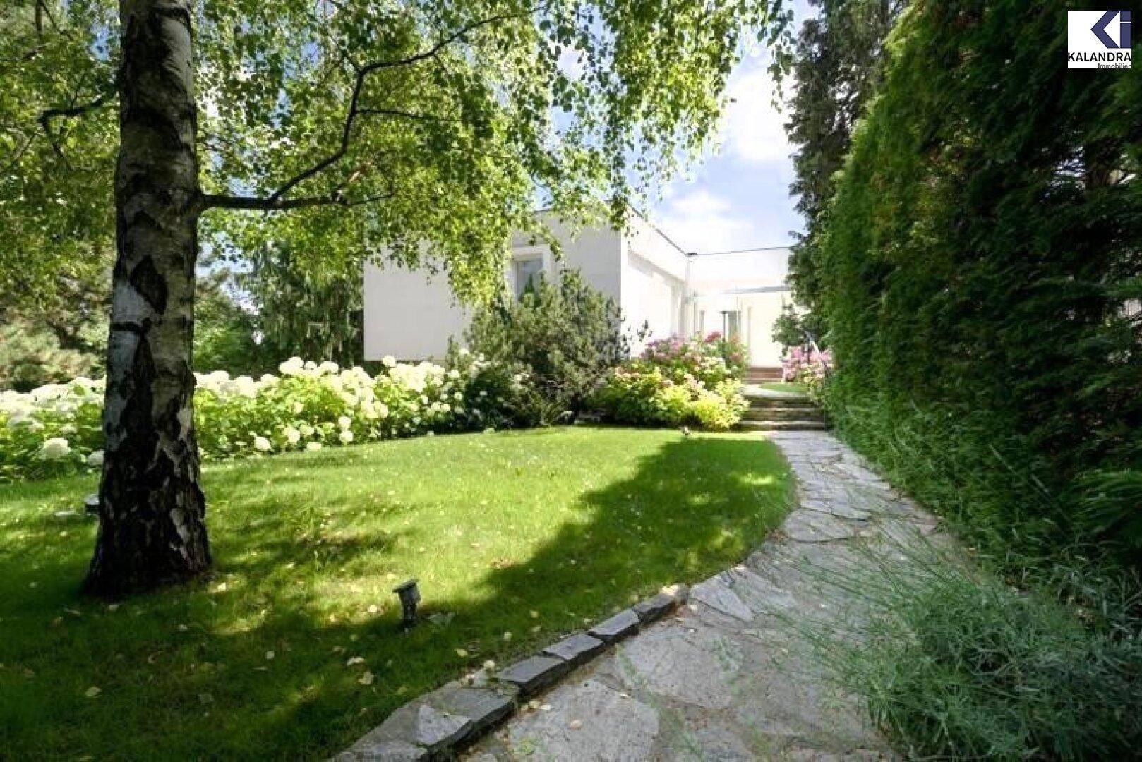 Geschwungener Steinweg durch den grünen Garten mit altem Baumbestand.