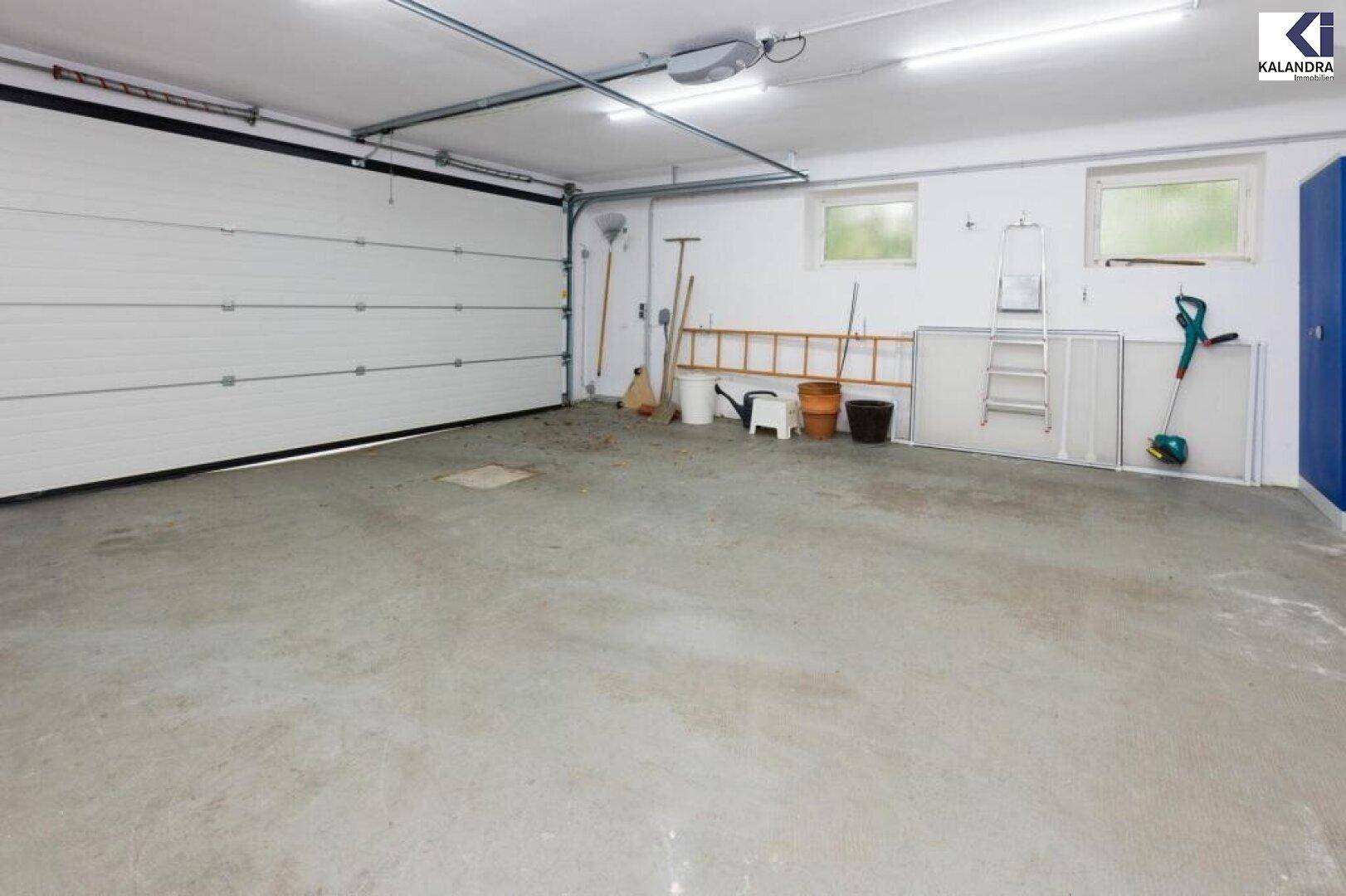 Geräumige Garage mit Betonboden, Fenstern und Stauraum für Gartengeräte.