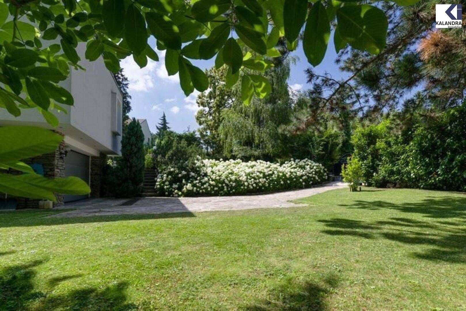 Weitläufiger grüner Garten mit Bäumen und blühenden Sträuchern.