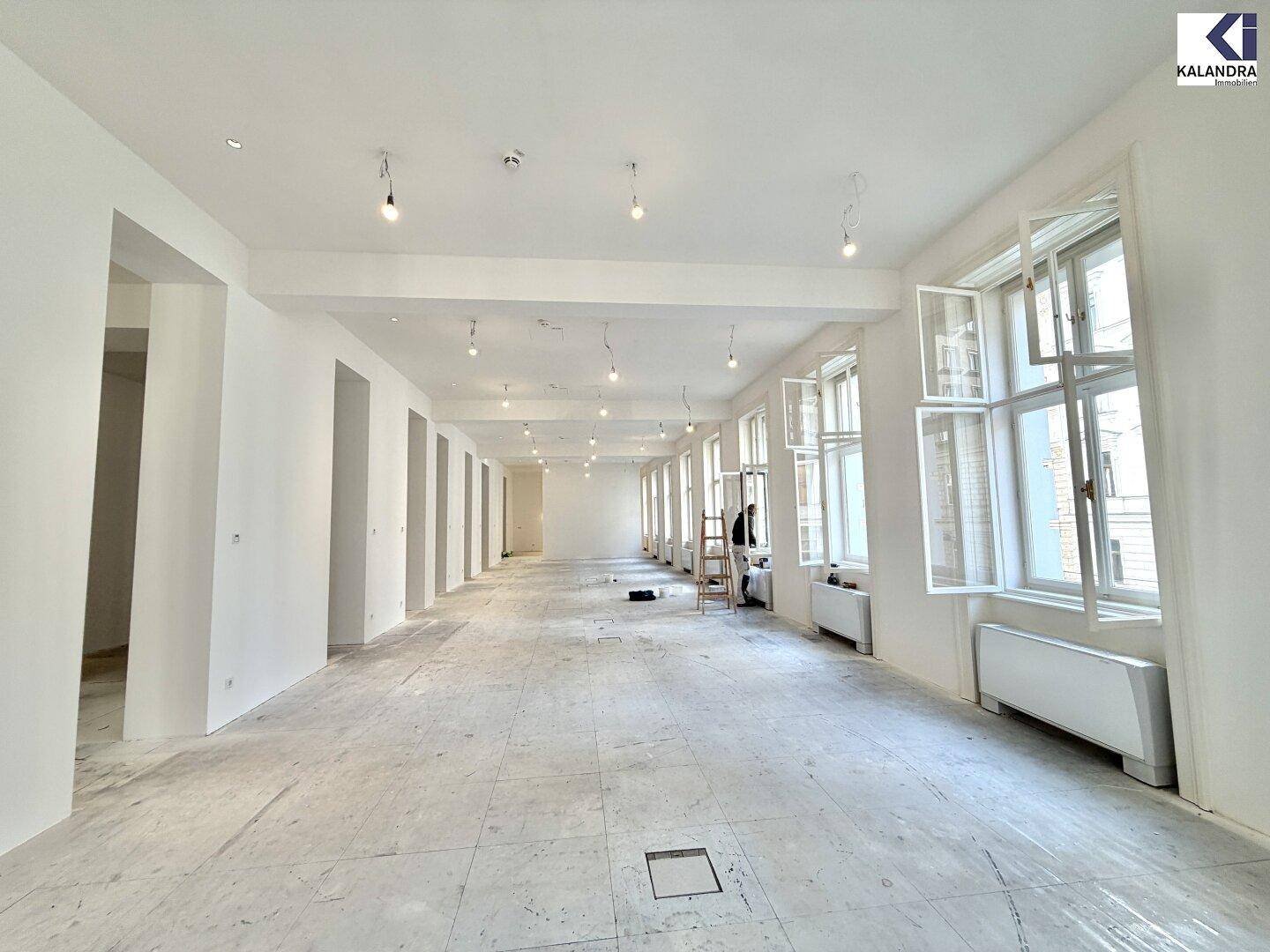 Weitläufiger, heller Büroraum mit vielen Fenstern und unfertigem Boden, ideal für flexible Raumgestaltung.
