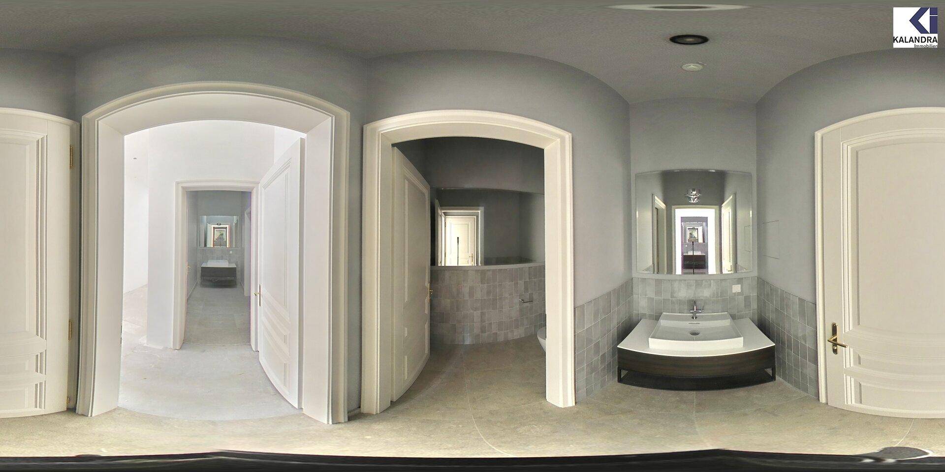 Geräumiges Badezimmer mit modernem Waschtisch, Spiegel und Zugang zu weiteren Räumen, in Grautönen.