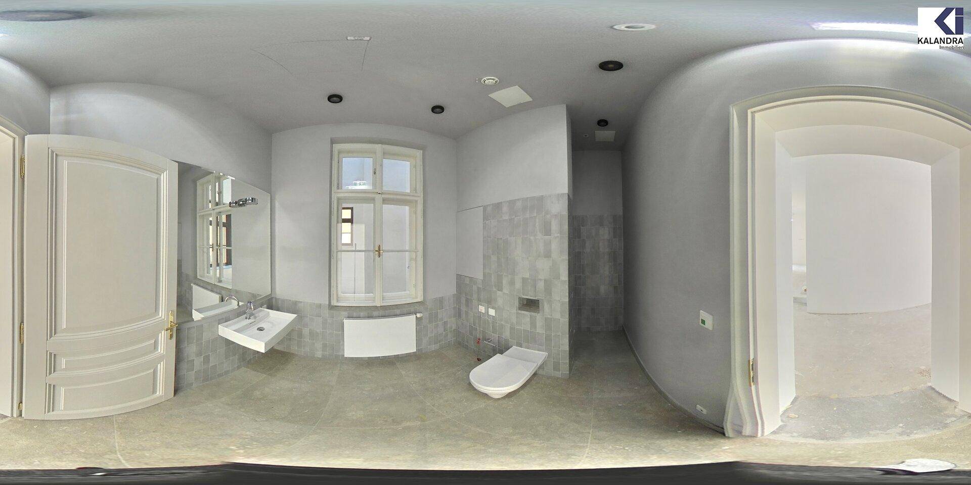 Modernes Badezimmer mit Fenster, Waschtisch und Toilette, in hellgrauen Fliesen ausgeführt und gut beleuchtet.