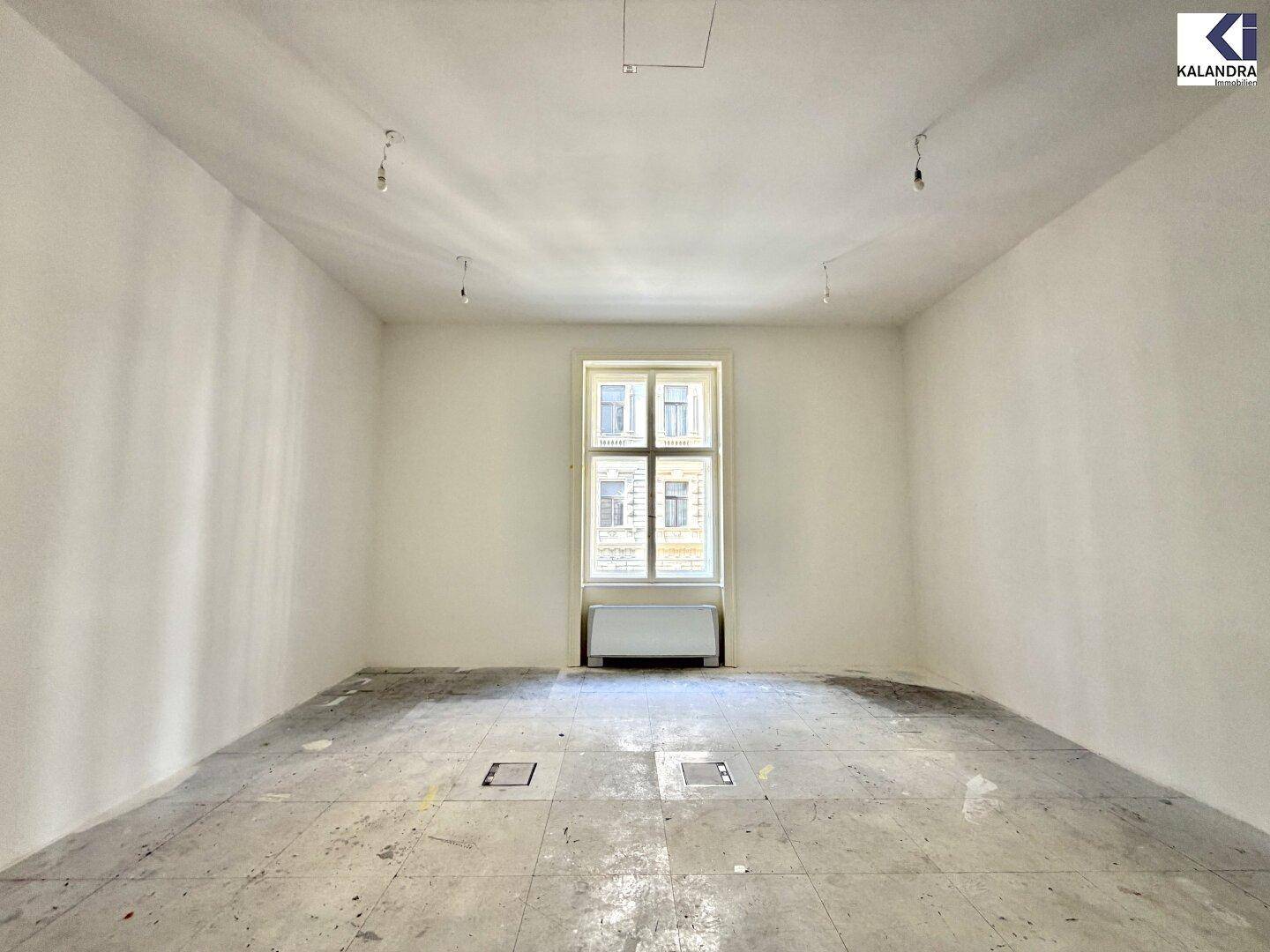 Heller Raum mit einem großen Fenster und hohen Decken, ideal für ein Einzelbüro oder Arbeitszimmer.