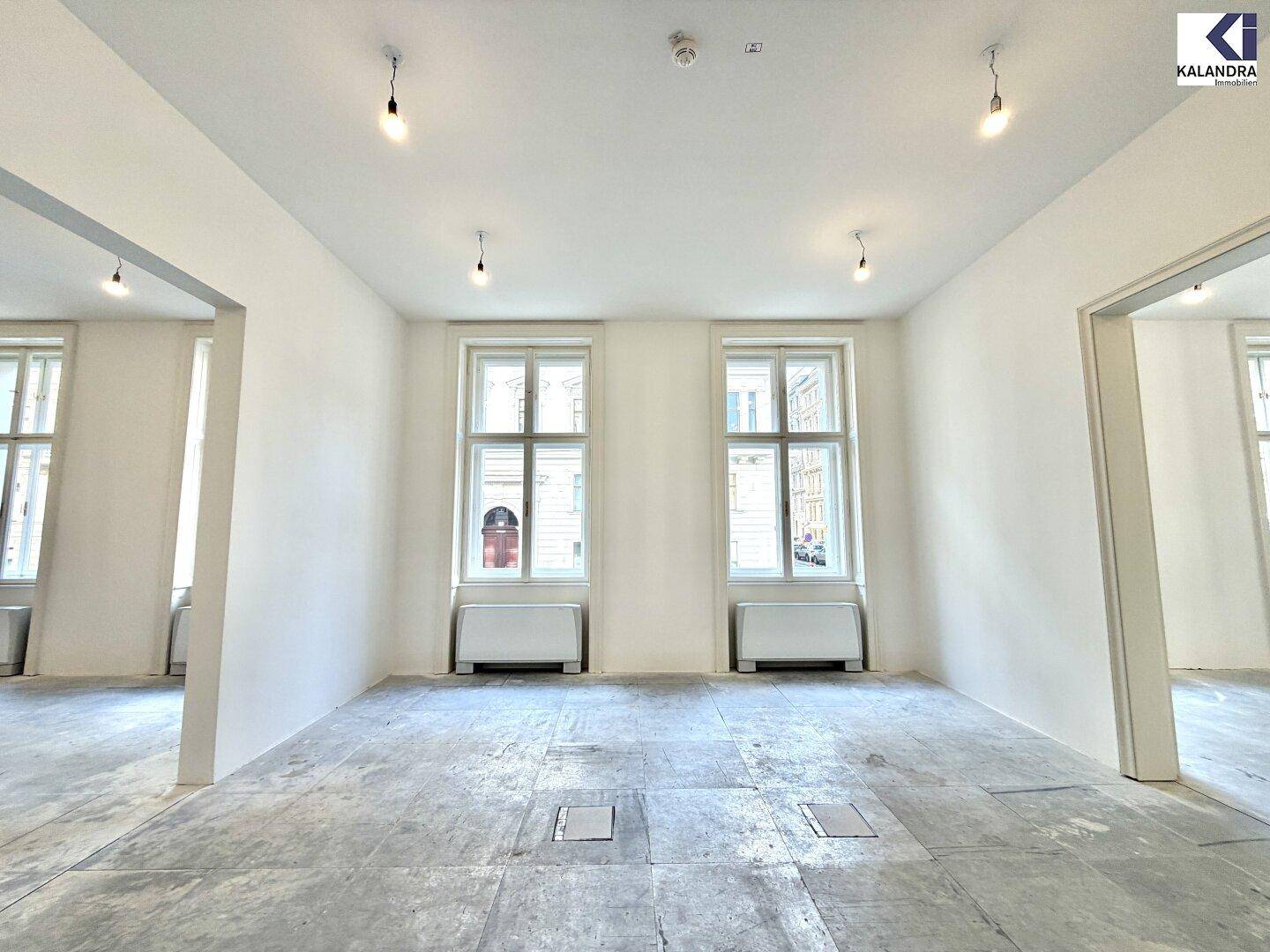 Heller Büroraum mit zwei großen Fenstern und einem unfertigen Boden, ideal für individuelle Gestaltung.
