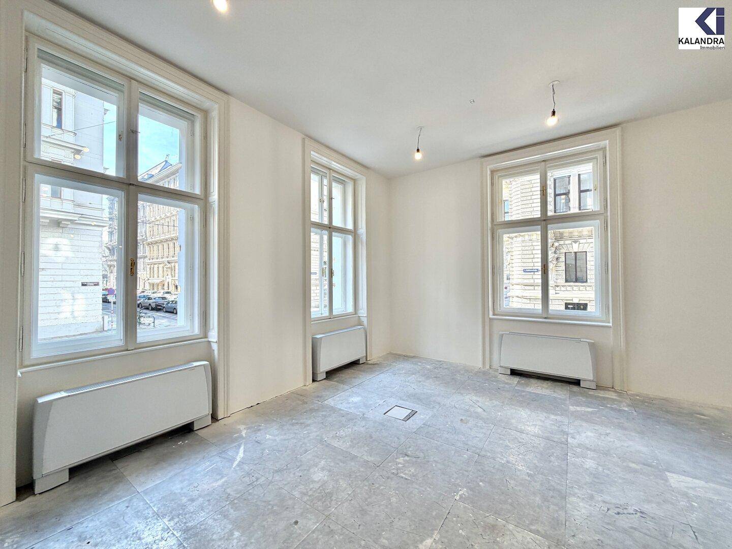 Eckbereich eines Büroraums mit drei großen Fenstern, die viel Tageslicht hereinlassen.