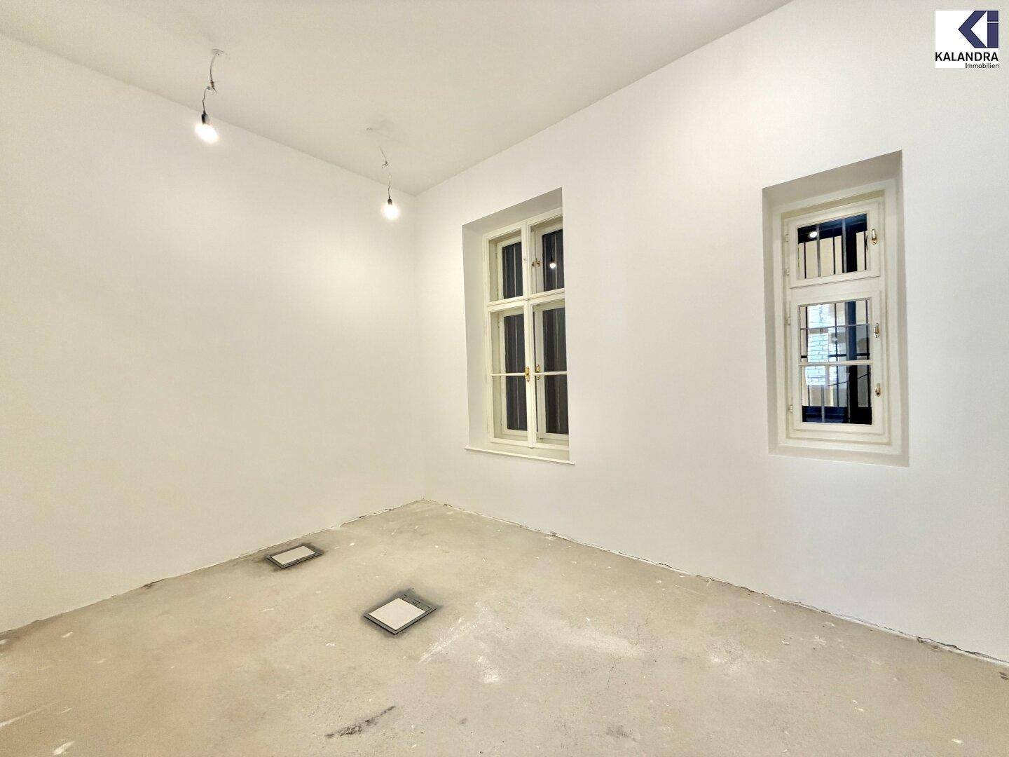 Kleinerer Büroraum mit zwei Fenstern und unfertigem Boden, ideal für individuelle Gestaltung.