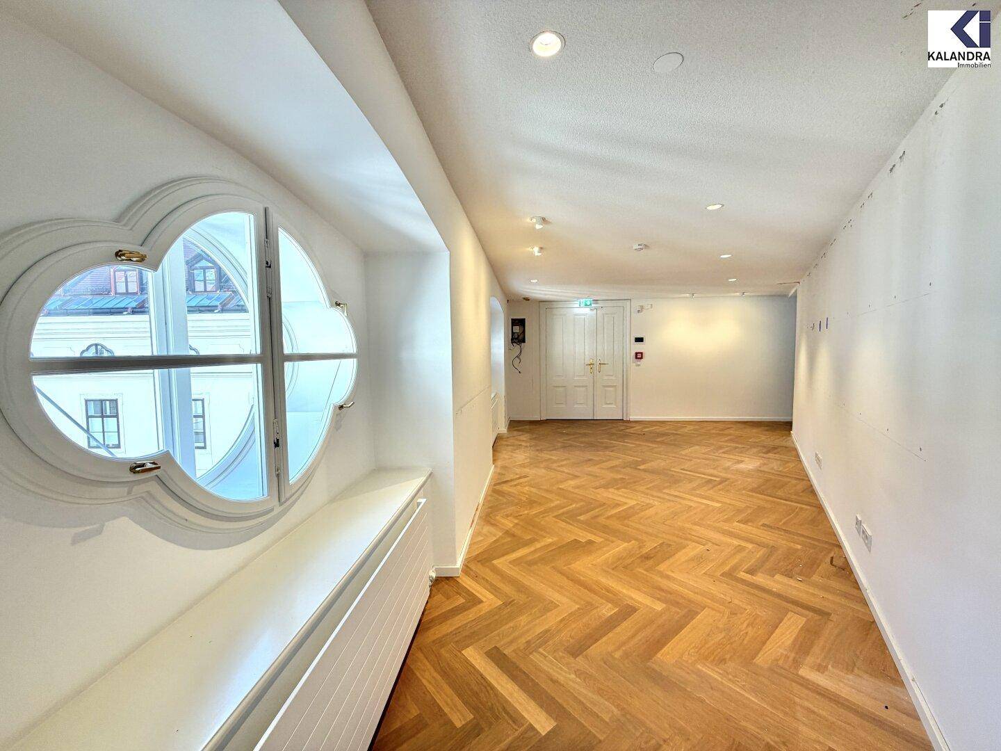 Heller Raum mit Fischgrätparkett und einem einzigartigen runden Fenster, das viel Licht spendet.