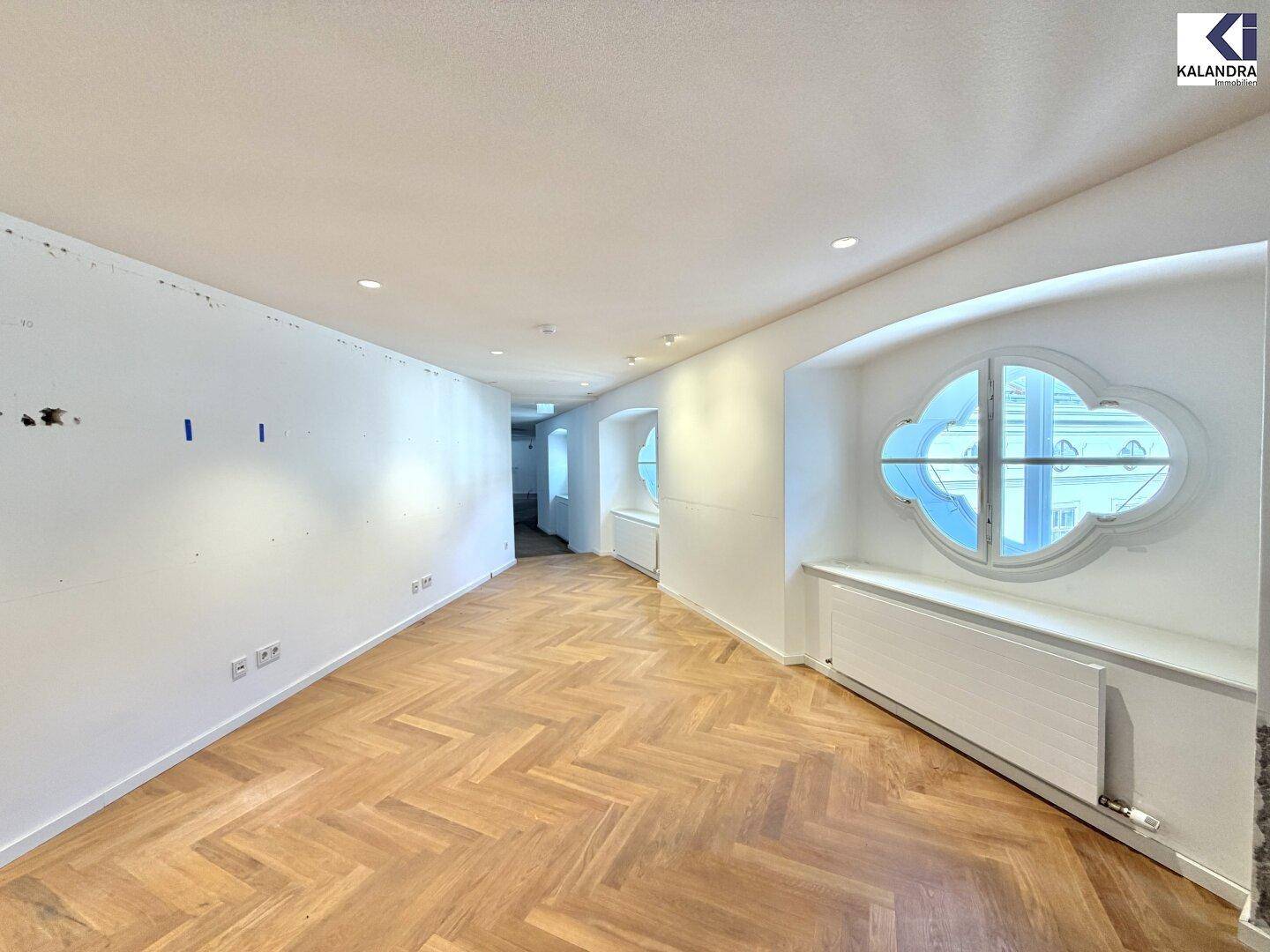 Heller Raum mit Fischgrätparkett und einem markanten Rundfenster, das viel natürliches Licht hereinlässt.