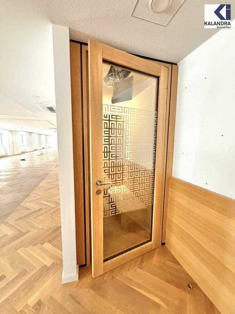 Moderne Holztür mit Glas und Muster, die zu einem kleinen, holzverkleideten Arbeitsbereich führt.