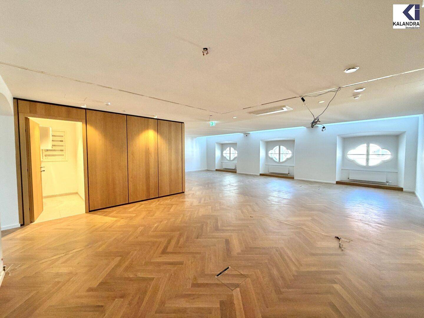Geräumiger, heller Raum mit Fischgrätparkett und einer modernen Holzvertäfelung, die einen Eingang verbirgt.