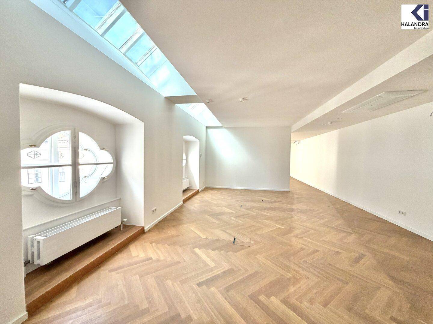 Heller Raum mit Fischgrätparkett und einem markanten Rundfenster, das viel natürliches Licht hereinlässt.