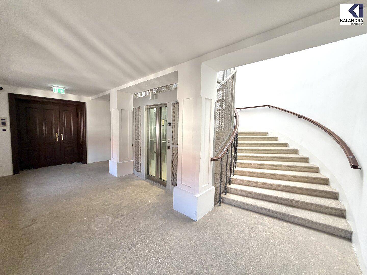 Eleganter Eingangsbereich mit Steintreppe, schmiedeeisernem Geländer und modernem Glasaufzug.