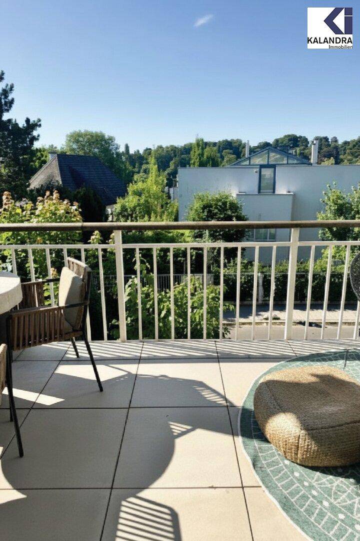 Sonniger Balkon mit Fliesenboden und Blick auf grüne Bäume und Häuser.
