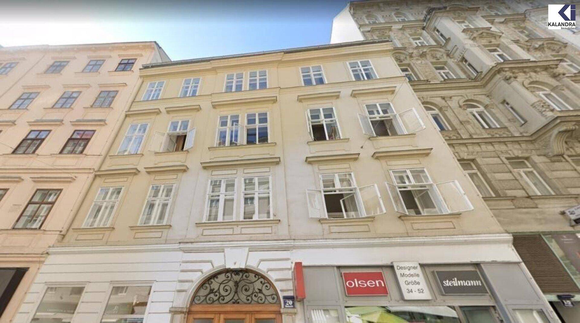 Historische Fassade eines Mehrfamilienhauses mit vielen Fenstern und Geschäften im Erdgeschoss, typisch für die Stadtansicht.