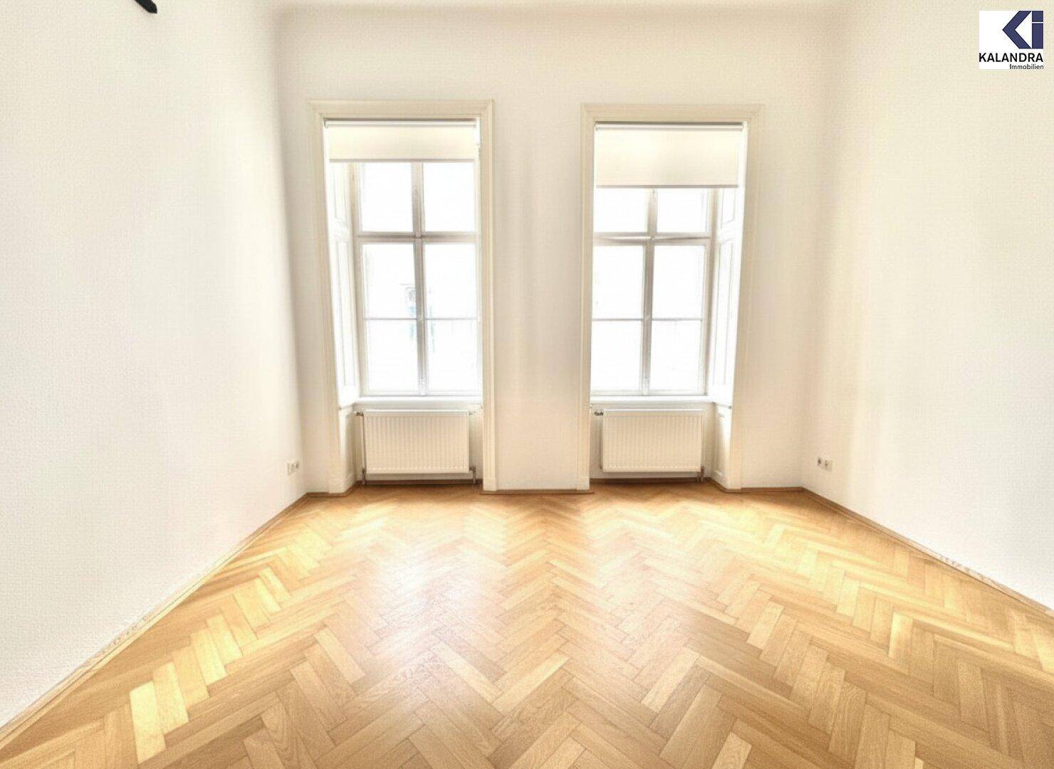 Heller Raum mit elegantem Fischgrätparkett und zwei Fenstern, ausgestattet mit modernen Rollos.