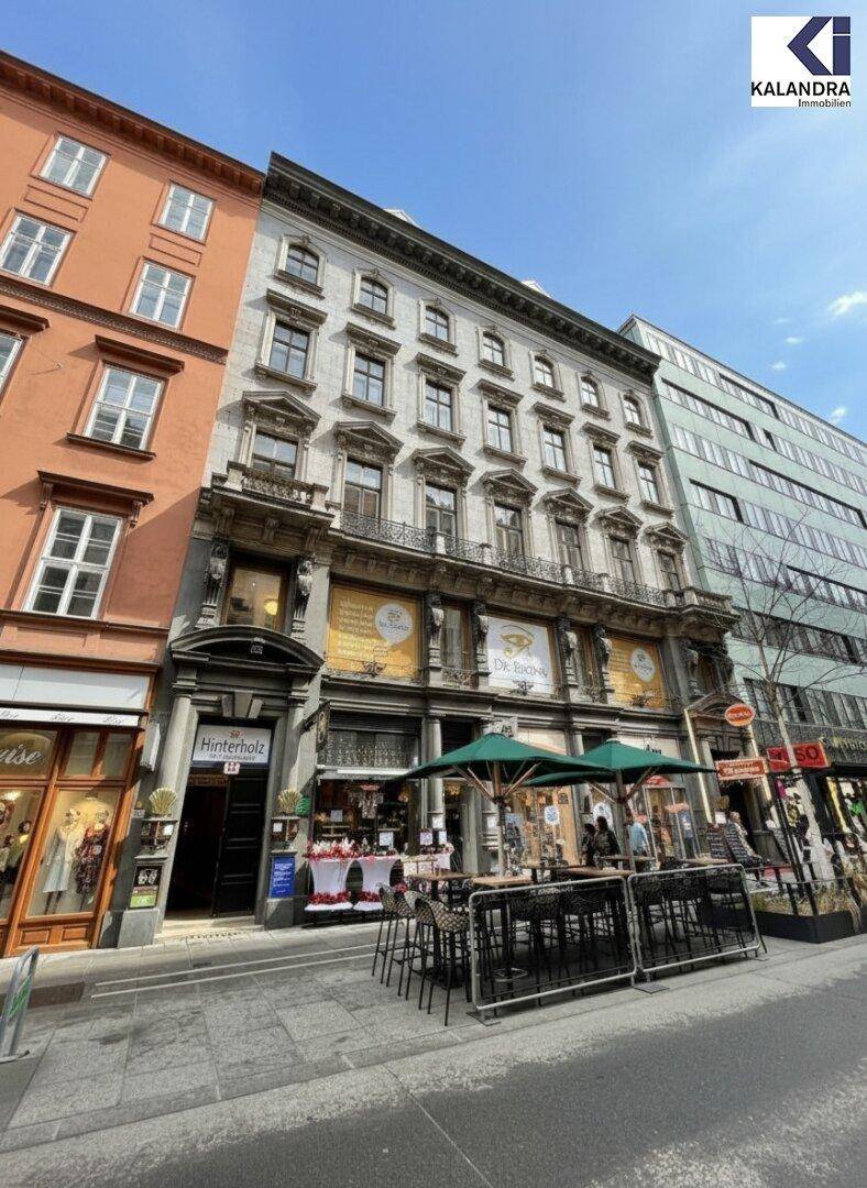 Historisches Gebäude mit reich verzierter Fassade und Geschäften im Erdgeschoss an einer belebten Straße.
