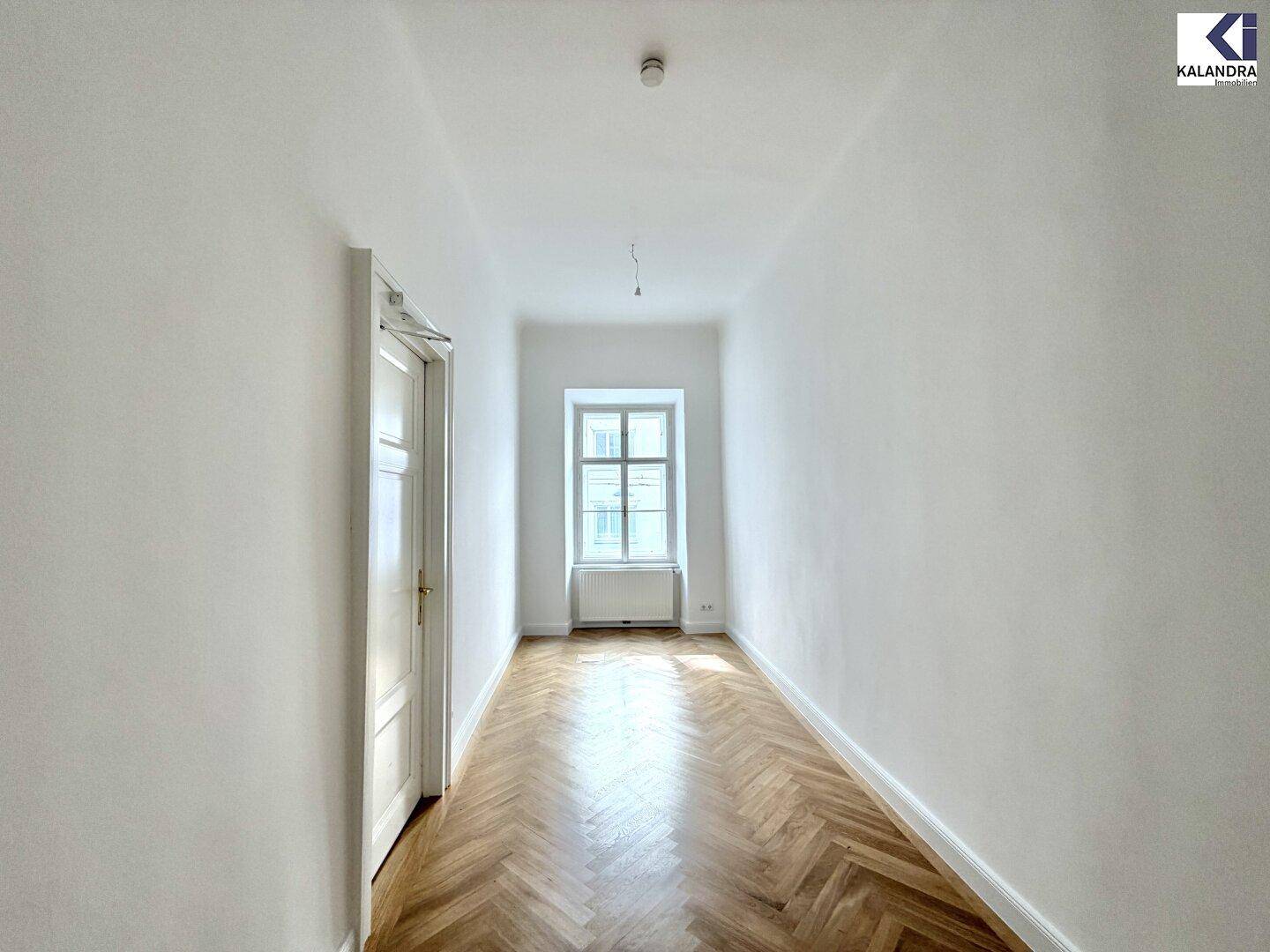 Langer, heller Flur mit elegantem Fischgrätparkett und einem Fenster am Ende, das den Raum mit Tageslicht erhellt.