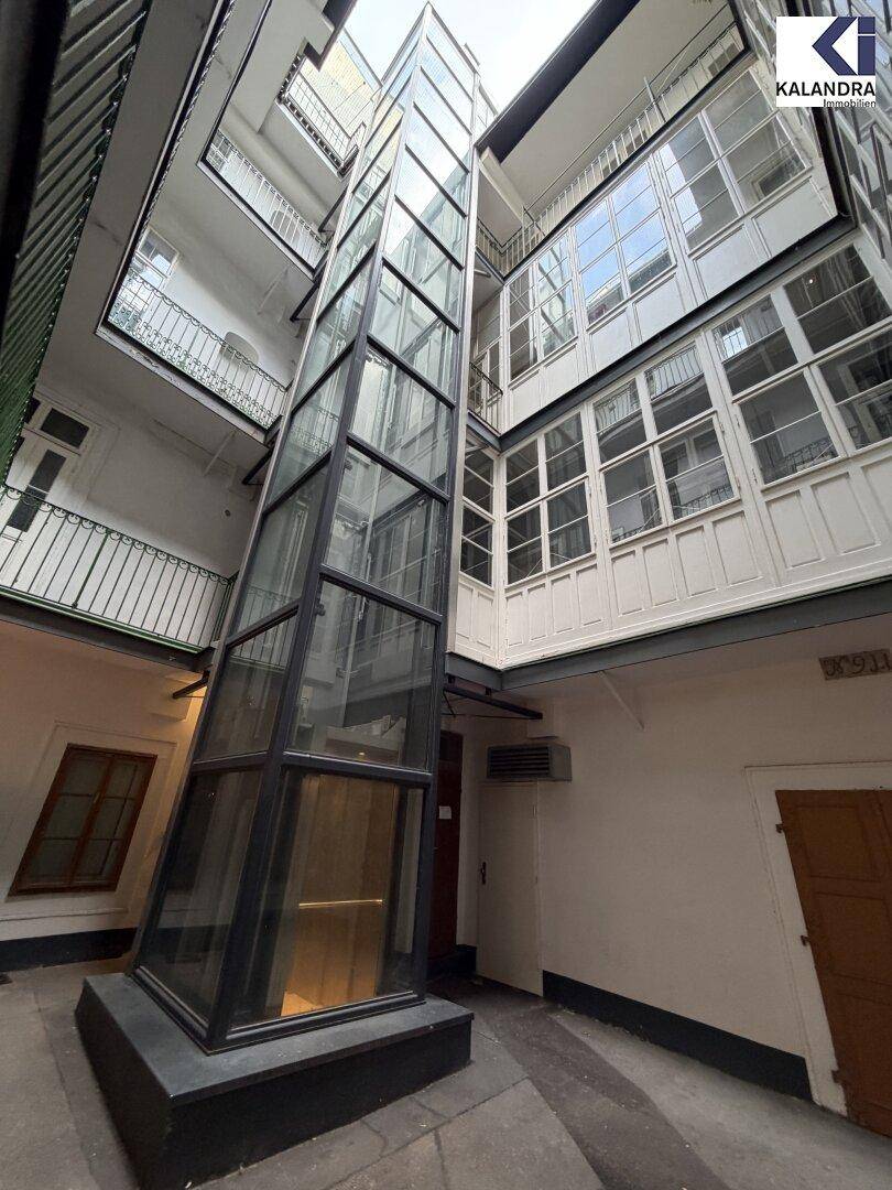 Innenhof eines Altbaus mit einem modernen Glasaufzug, der die oberen Etagen erschließt.