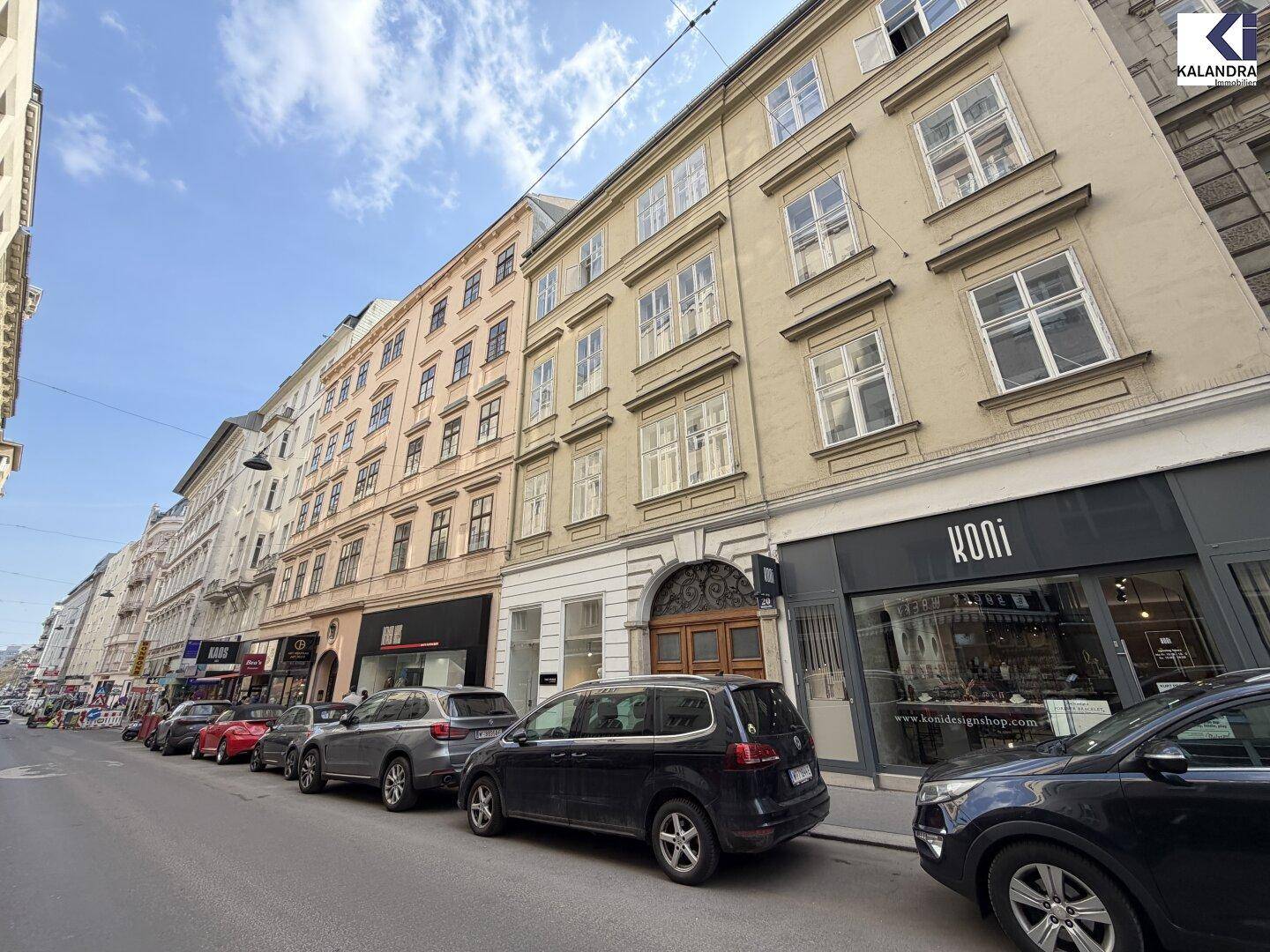 Straßenansicht eines historischen Gebäudes mit Geschäften im Erdgeschoss und parkenden Autos davor.