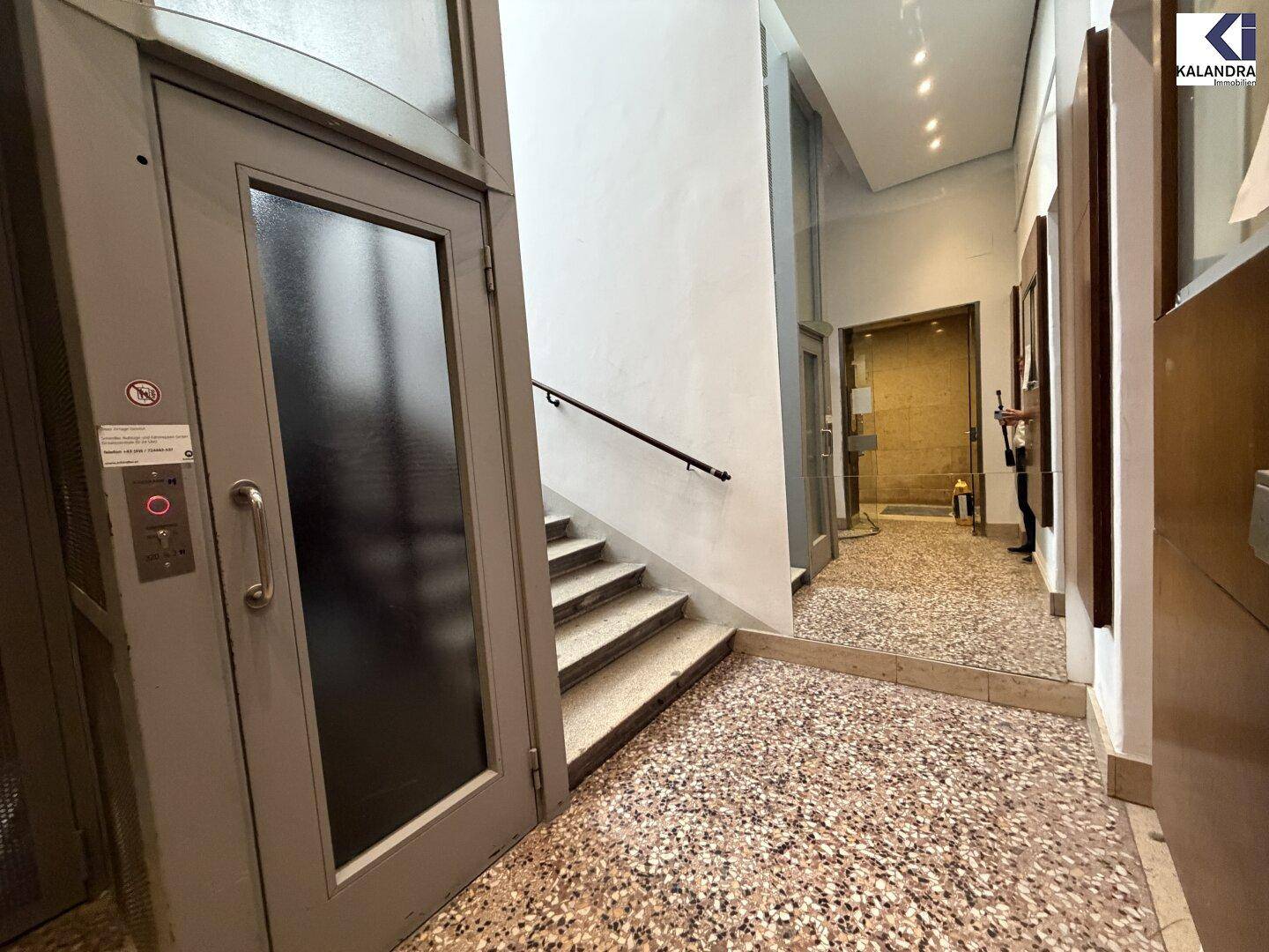 Eingangsbereich mit Aufzug, Treppe und Terrazzoboden, der Zugang zu den oberen Etagen bietet.